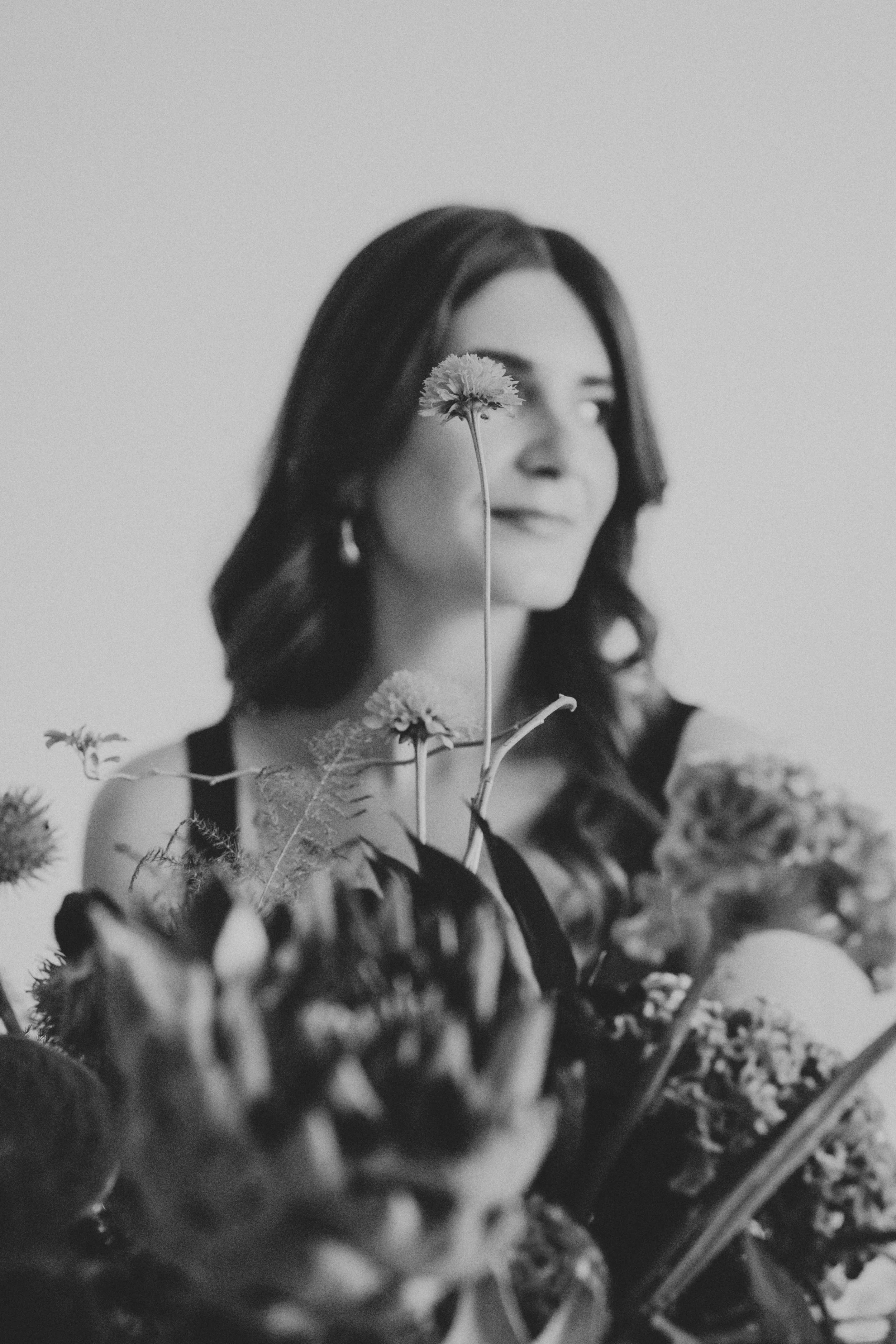 Portrait en noir et blanc d'une femme avec des fleurs devant le visage.