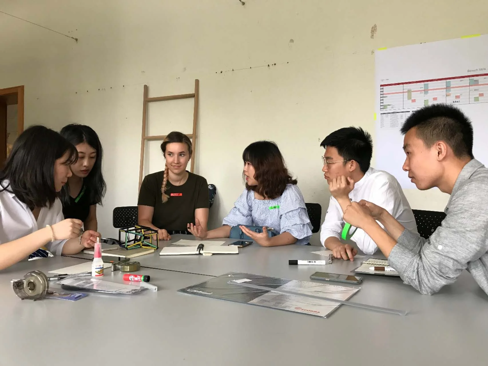 Six people sitting at a conference table having a discussion, with various documents and stationery on the table.