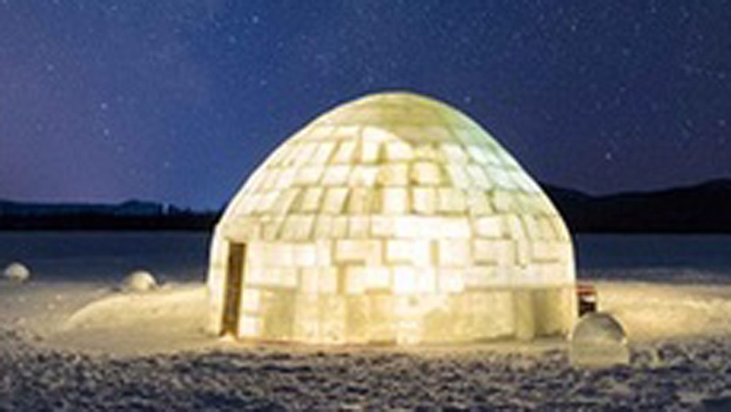 An illuminated dome-shaped structure made of tan bricks, situated outdoors at night, with a dark sky and distant hills in the background.