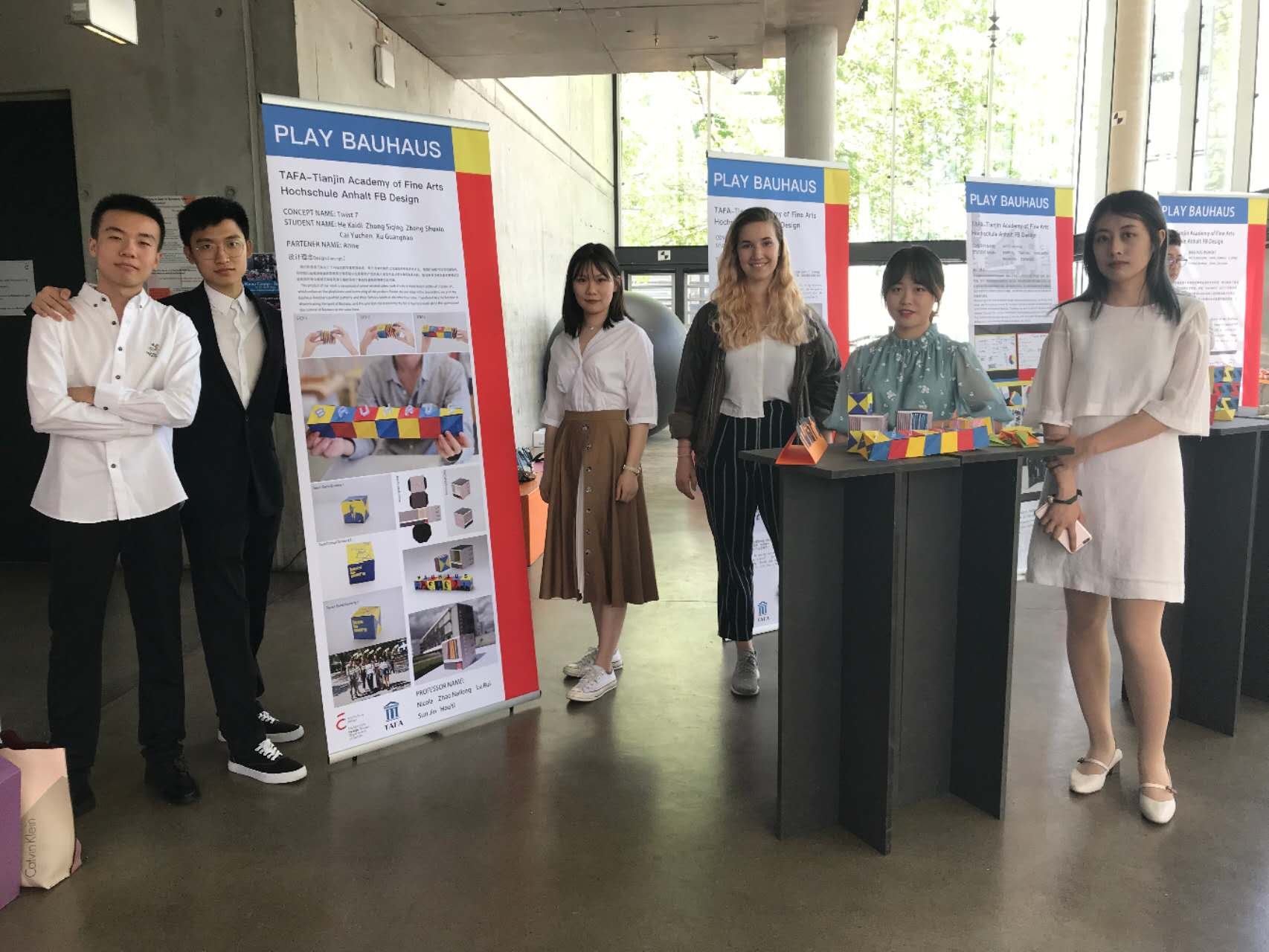 Group of six students presenting at a booth about Bauhaus design, with posters and colorful craft projects displayed.