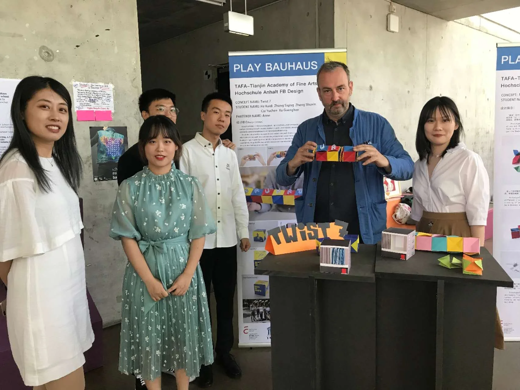 Group of six people at an exhibition booth with colorful paper models and a sign that reads 'TWIST'.