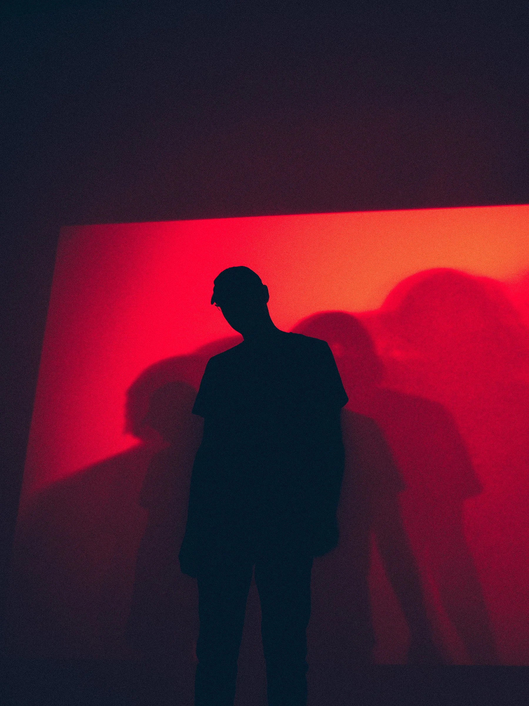 Silhouette of a person standing in front of a lit red background, casting shadows on the wall.