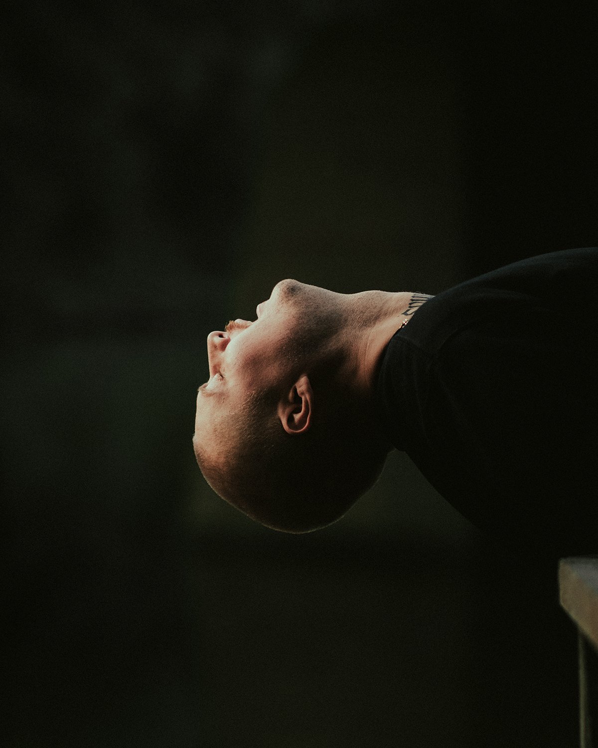 Side profile of a man with a shaved head, looking upward with a dark background.