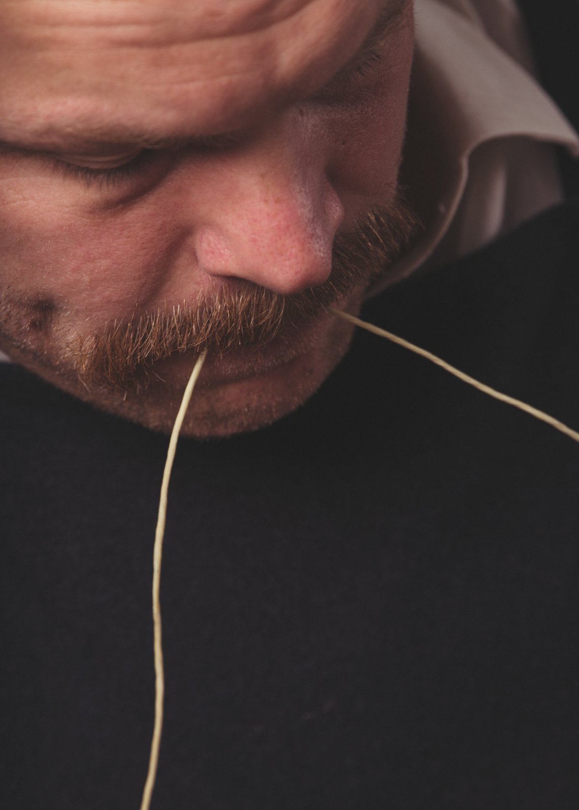 Extreme close-up of shoemaker holding the tip of a waxed thread in his mouth.