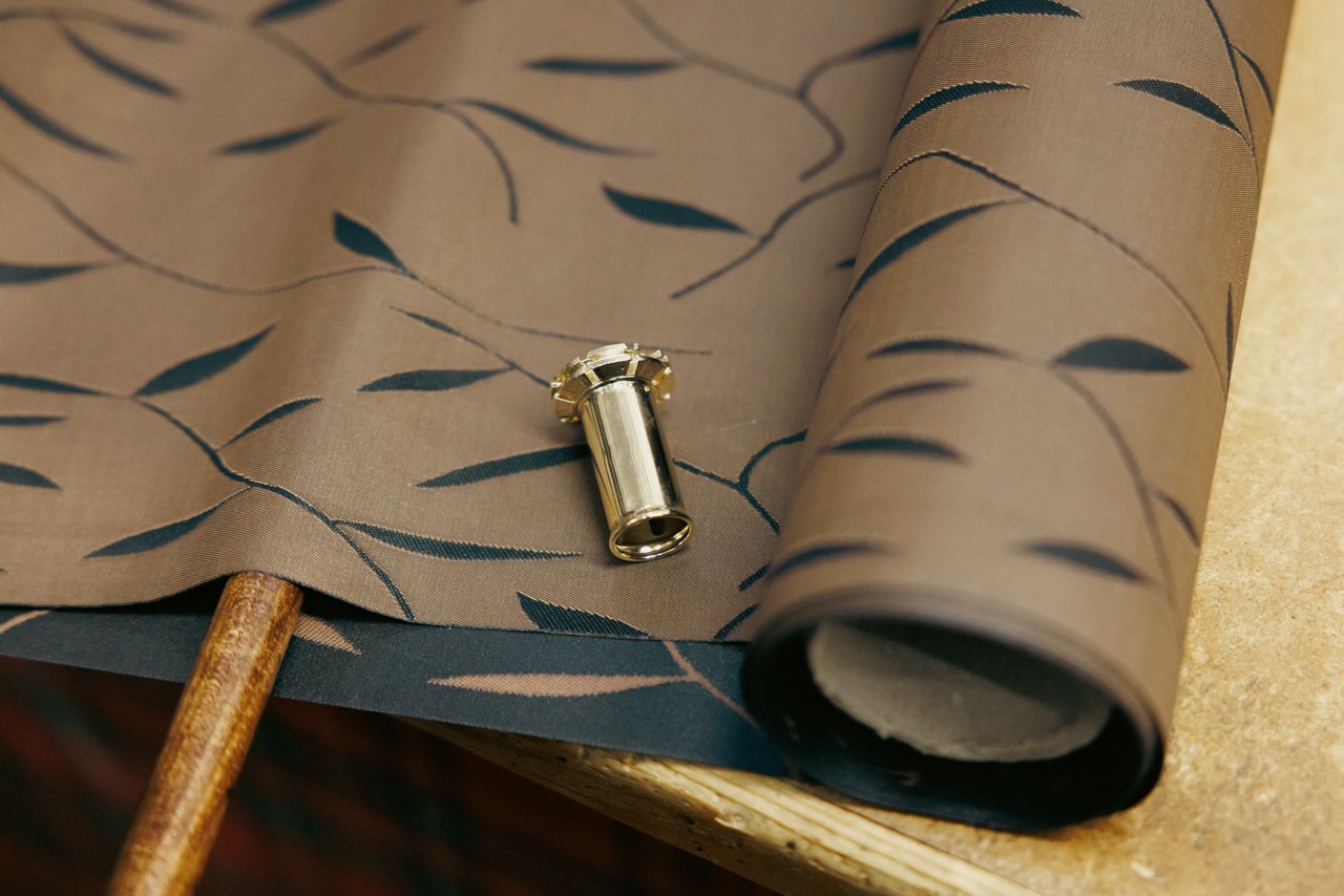 Close-up of patterned umbrella fabric with a polished metal tip component resting on it.