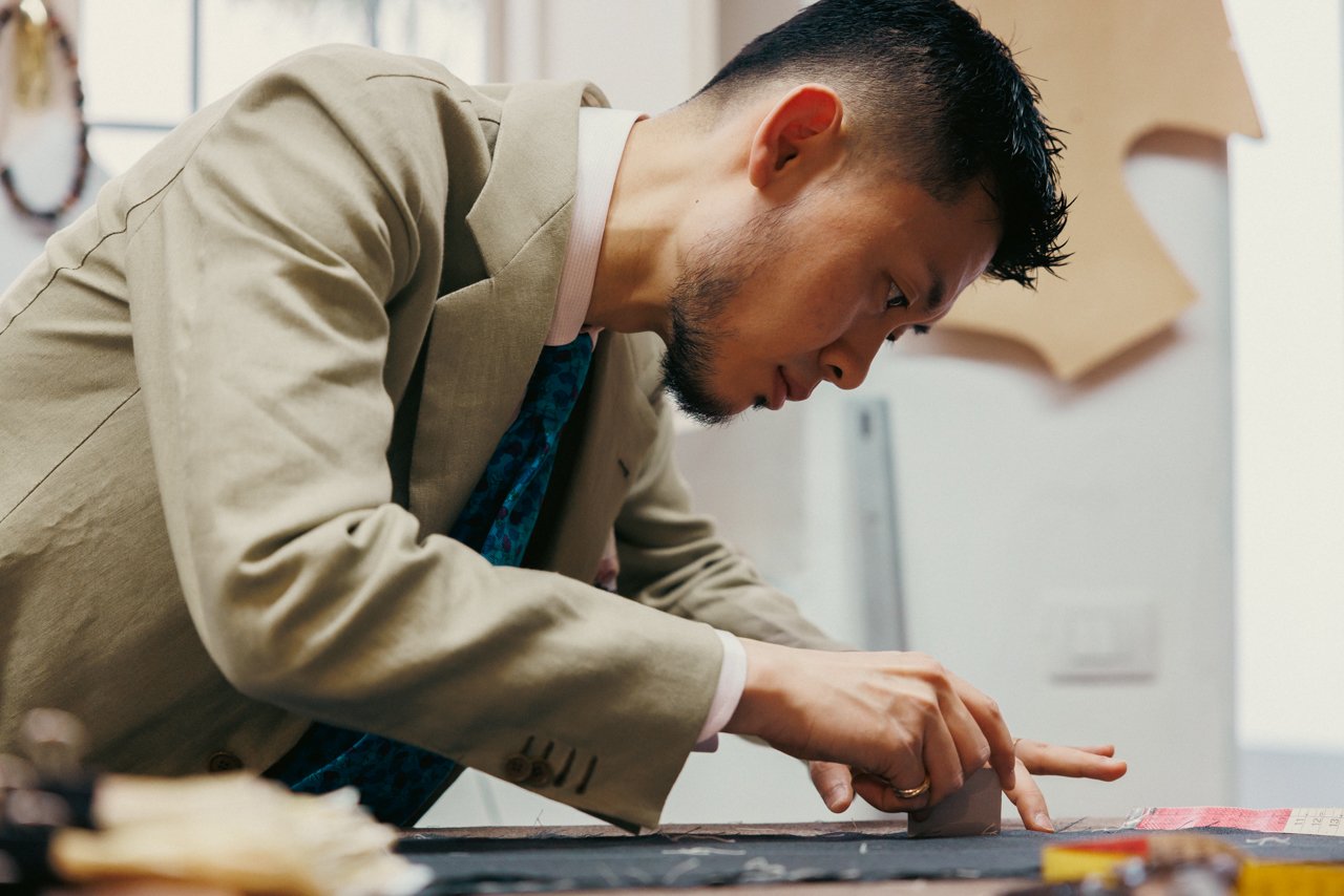 Liverano tailor Takahiro Osaki marking or cutting fabric at a workbench.