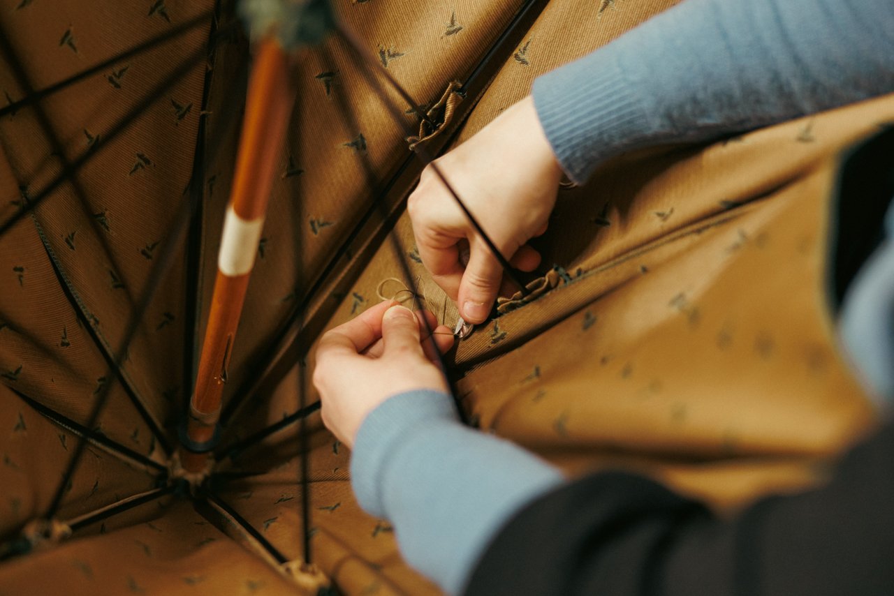 Close-up of hands carefully securing the lining fabric to the interior ribs of an umbrella frame.