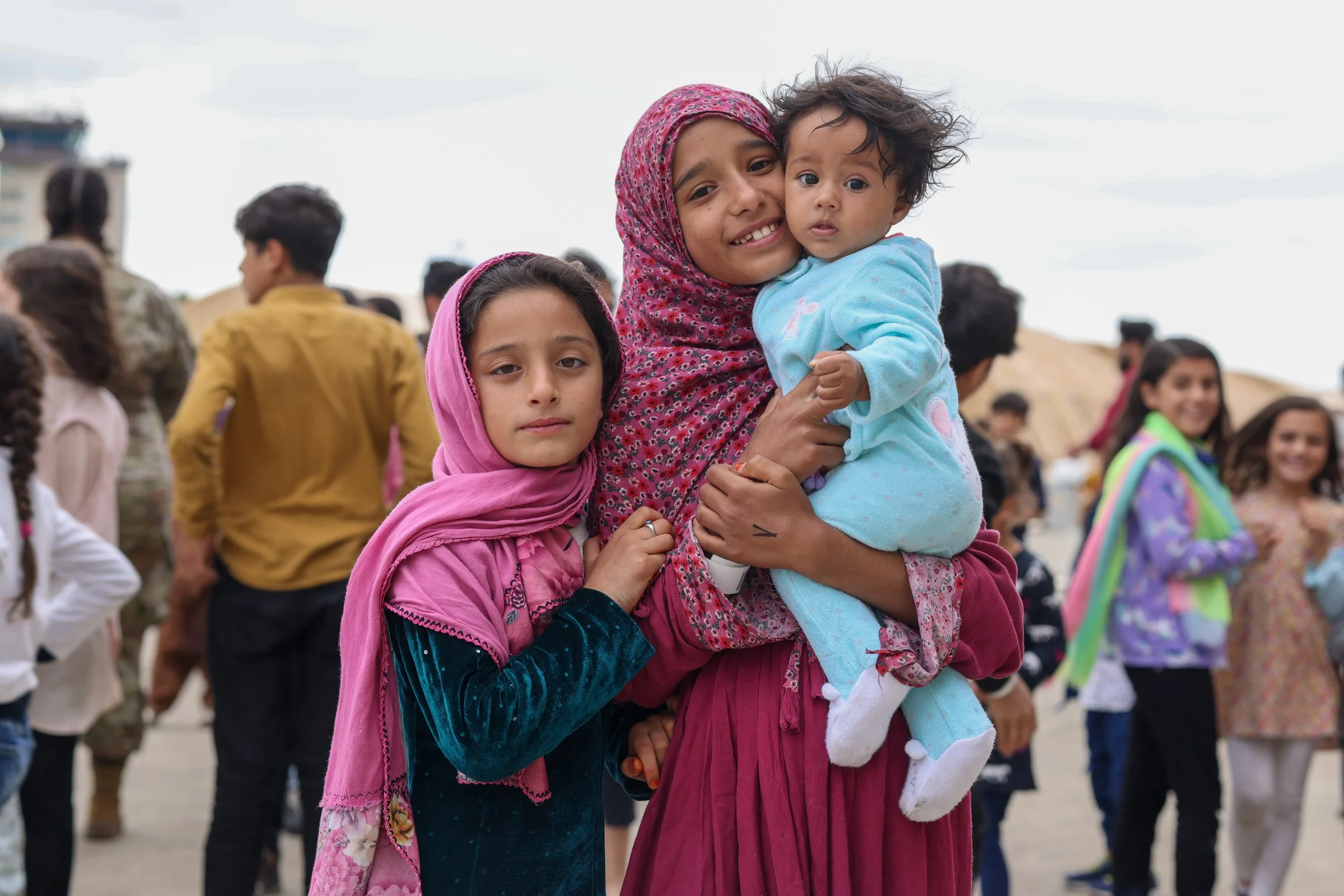 A group of Afghan children and women, some wearing headscarves, gathered outdoors  in Ramstein American Airbase in Germany.