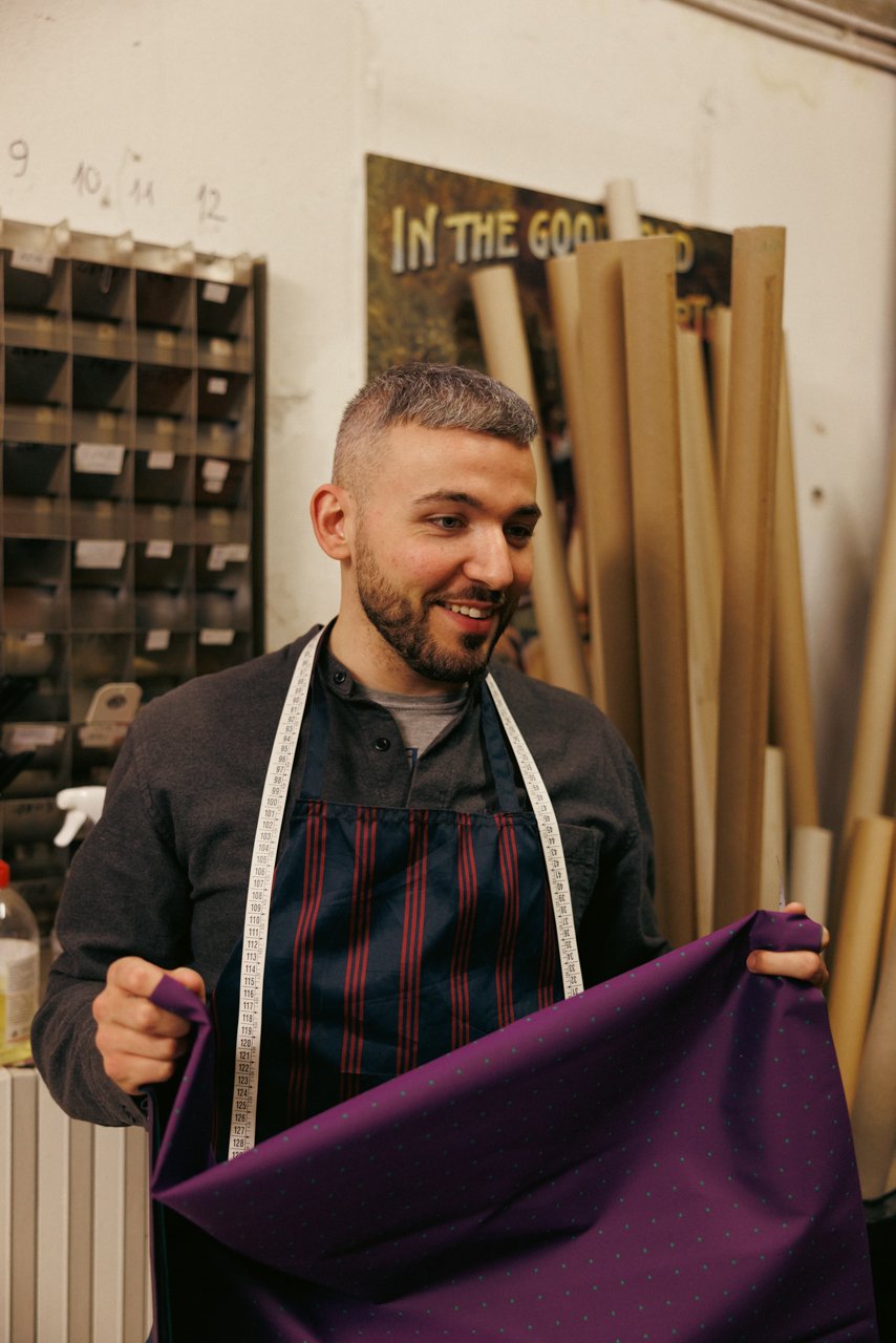 Smiling Francesco Maglia displaying a piece of rich purple fabric in the workshop.