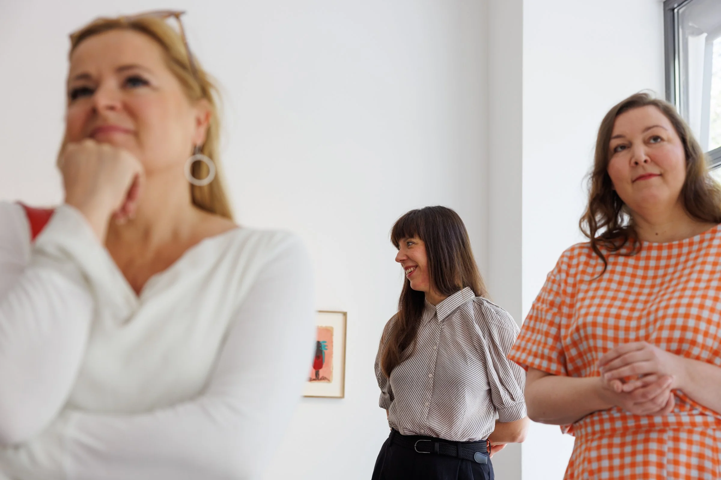 Four women standing together in an art gallery, smiling and engaging in conversation.
