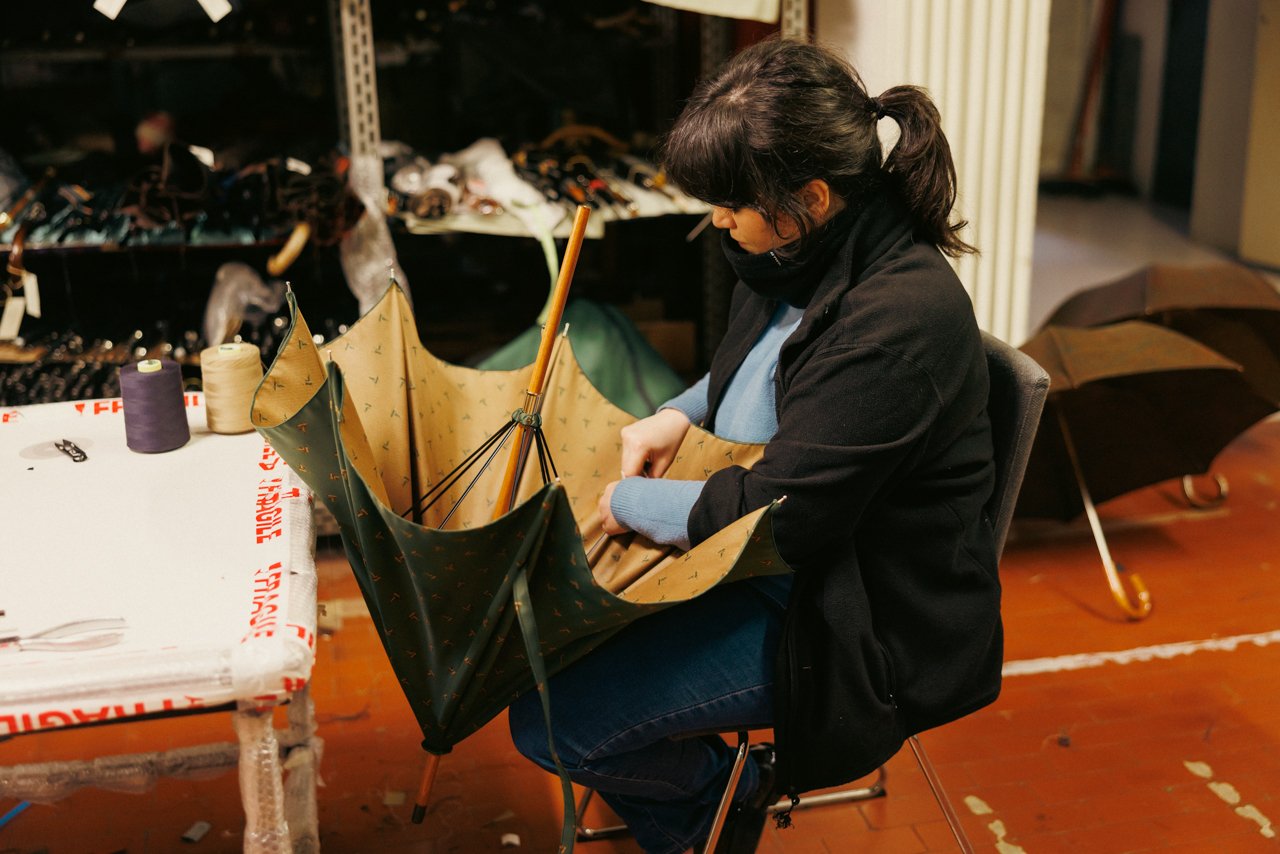 Woman meticulously hand-sewing the canopy panels onto the frame of an umbrella.