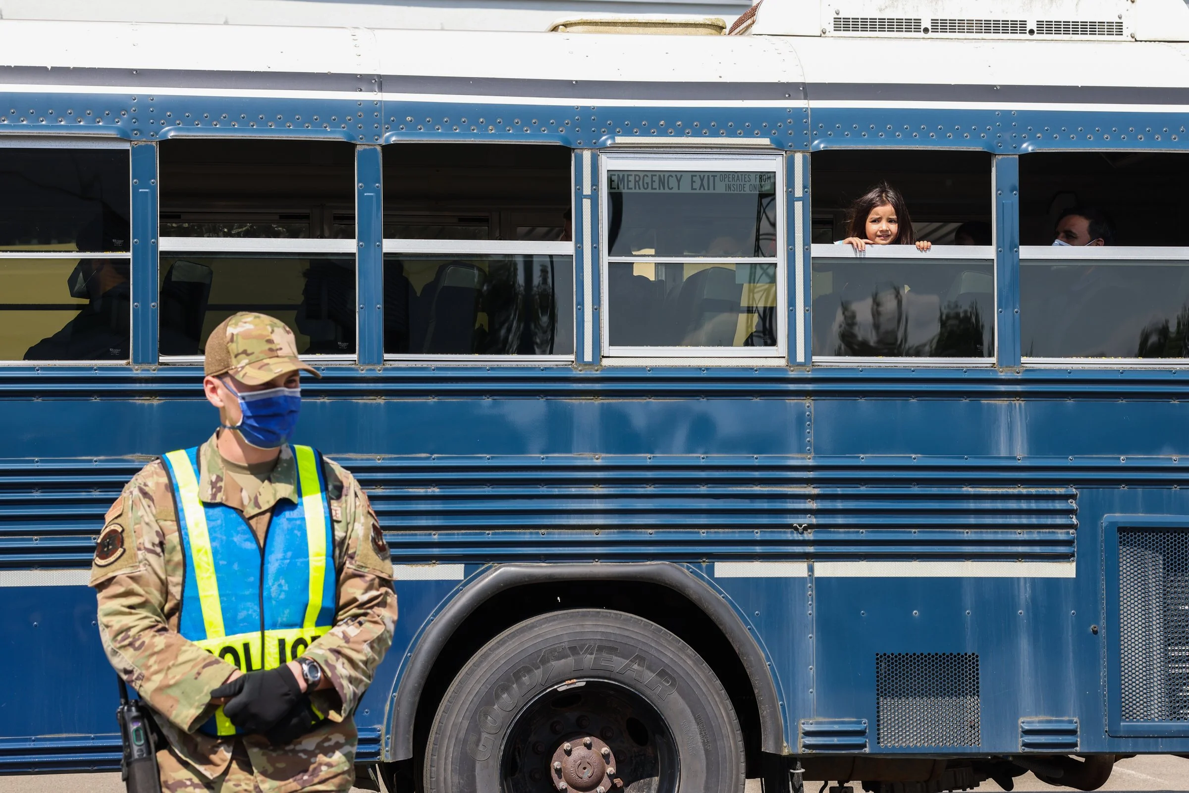 A young girl looks out from a school bus window as a police officer in camouflage uniform and a high-visibility vest stands in front of the bus in Ramstein American Airbase in Germany.