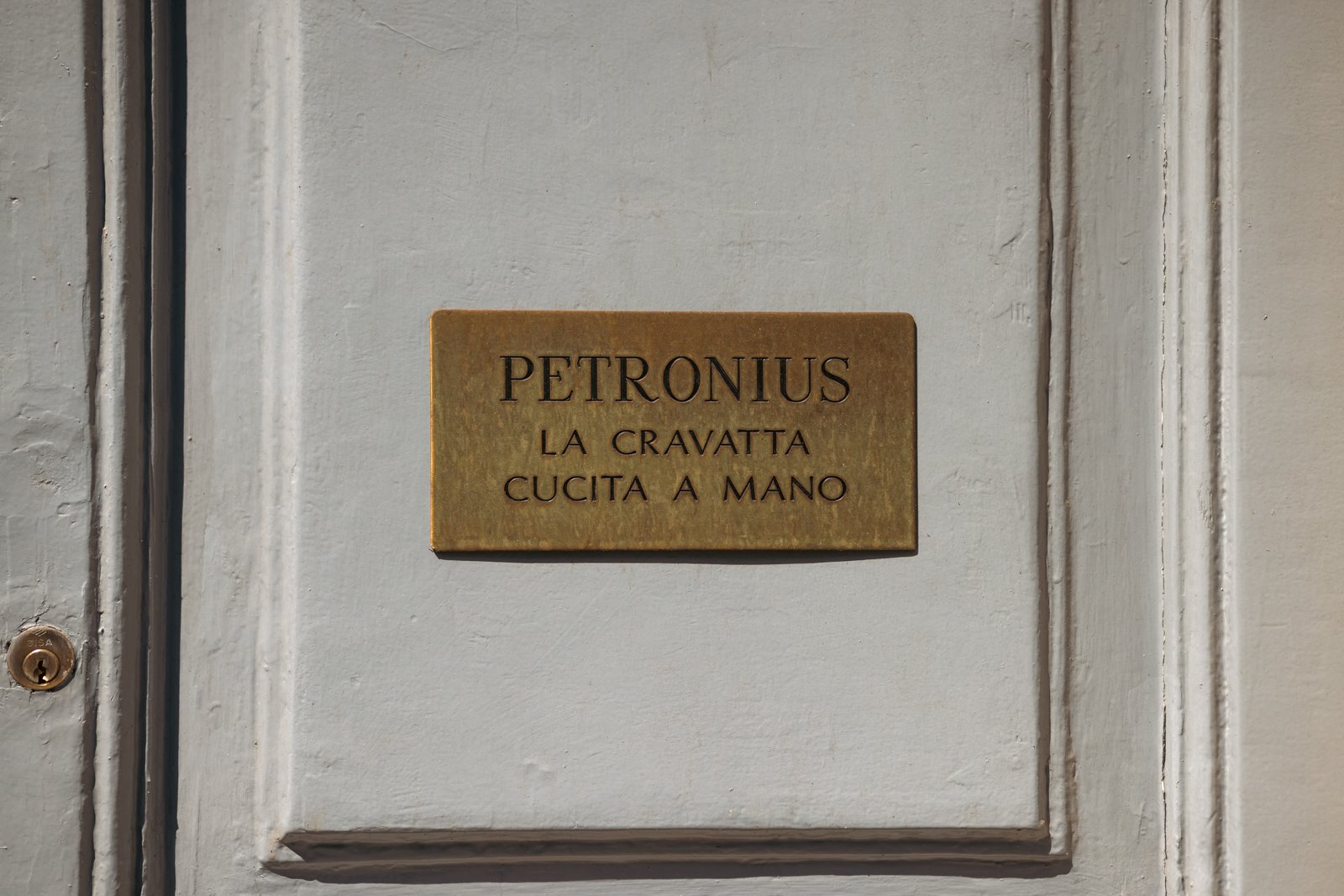 Close-up of the Petronius 1926 wall plaque stating "LA CRAVATTA CUCITA A MANO" (The Hand-Sewn Tie), signifying their core craft.