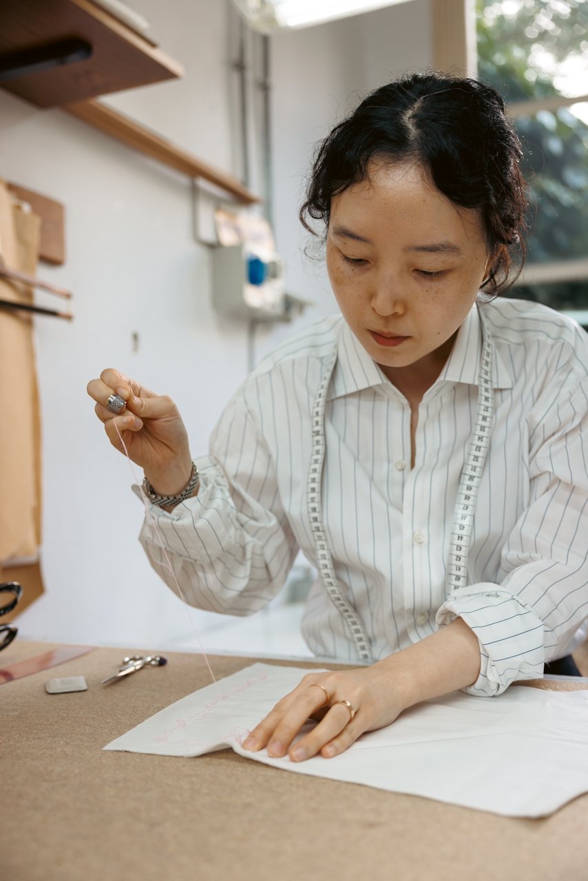 Female tailor focused on hand-sewing at her workstation.