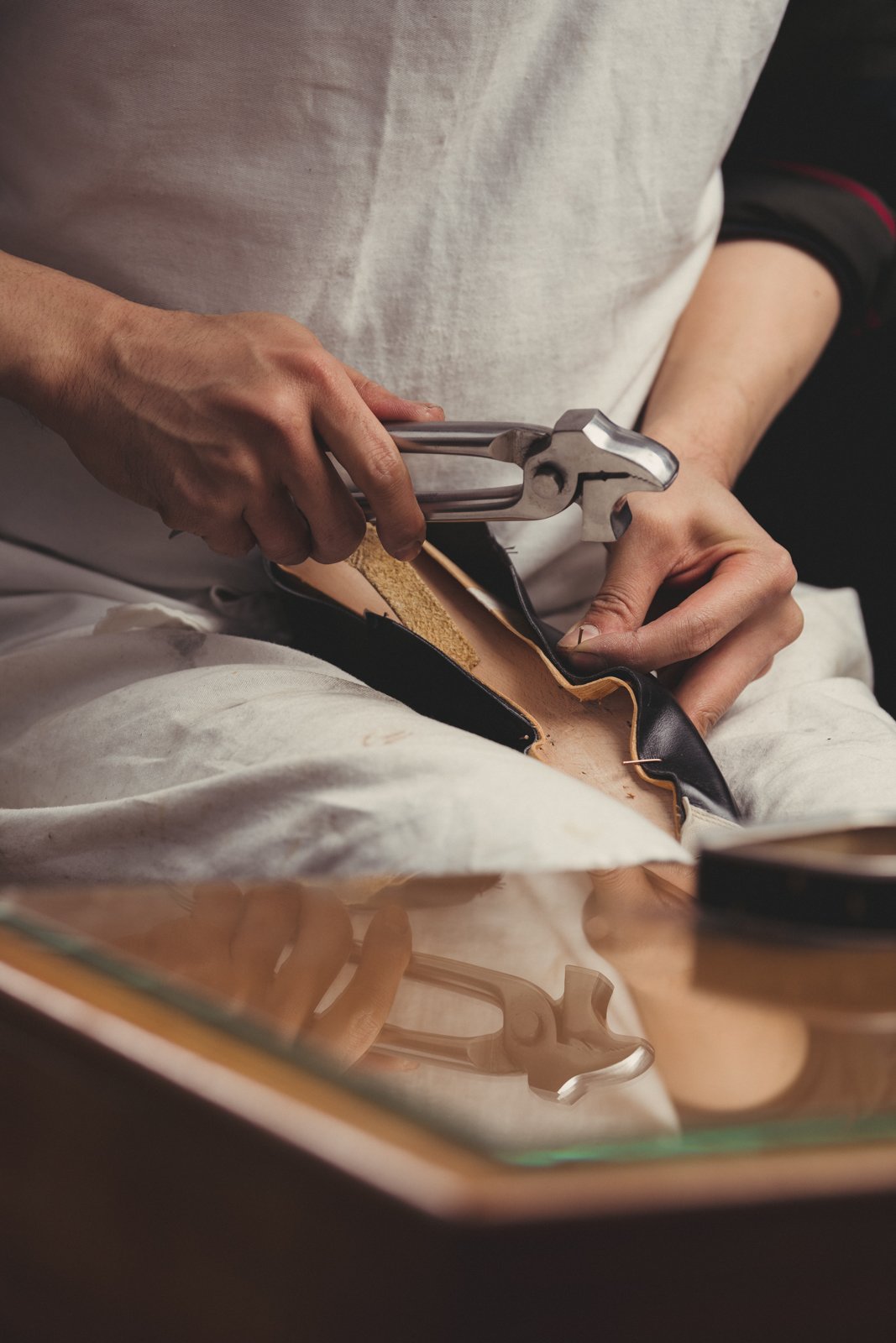 Shoemaker in apron using lasting pincers to stretch leather over a shoe last.