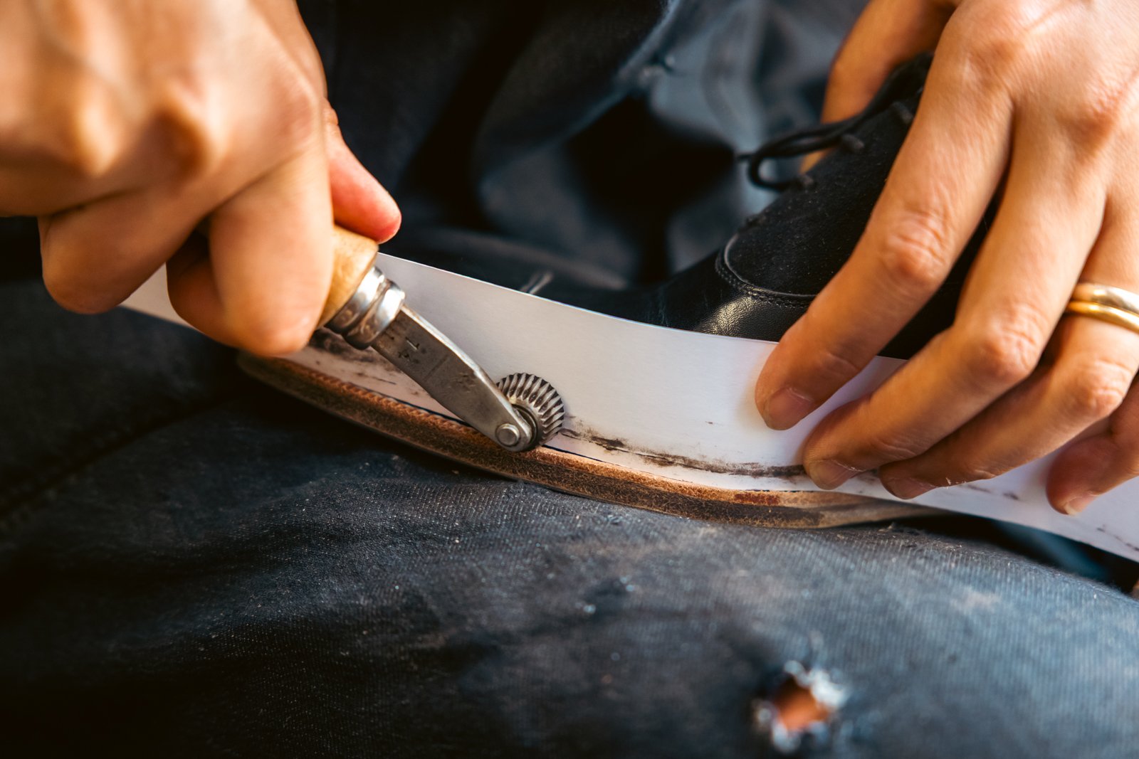 Close-up of a fudge wheel tool creating decorative impressions on the welt of a bespoke shoe, highlighting fine shoemaking details.