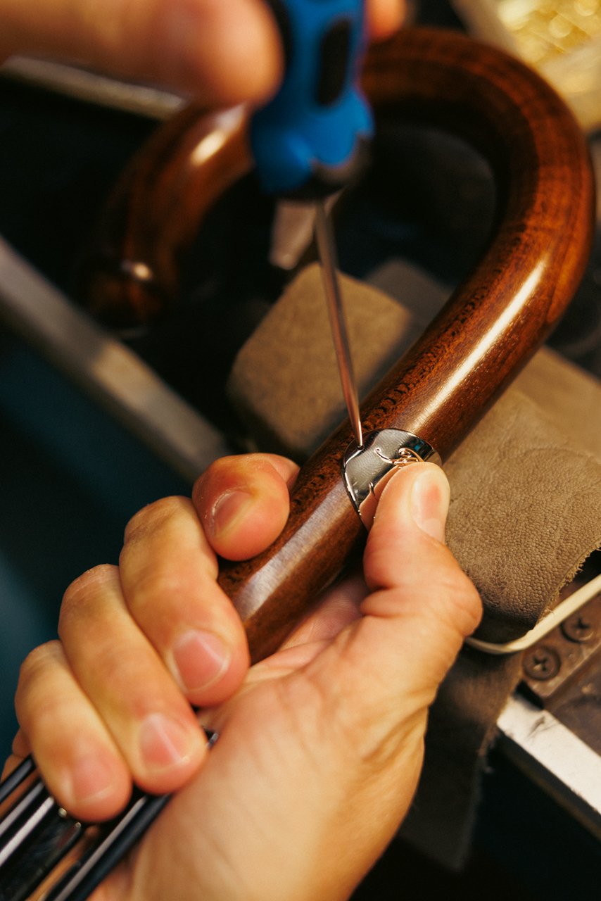 Detailed close-up of hands using a specialized tool to work on the fitting of a polished wooden umbrella handle.