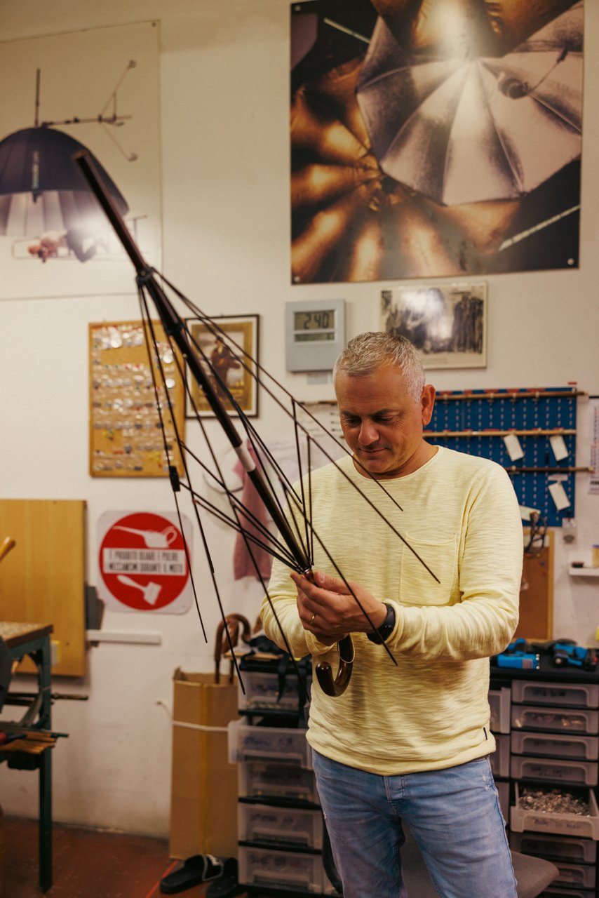 Man in a yellow sweater meticulously assembling or inspecting the complex rib structure of an umbrella frame.