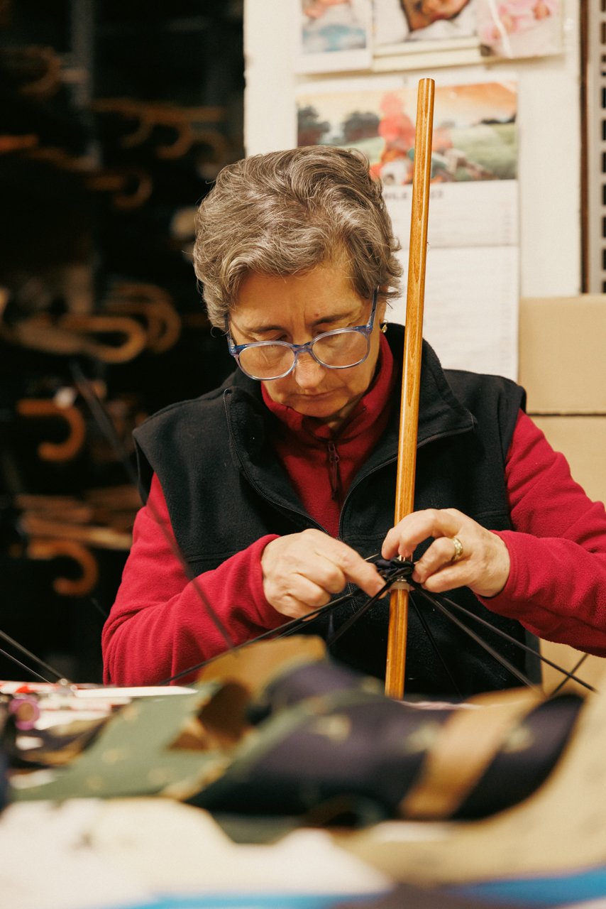Woman artisan concentrating on detailed assembly work on an umbrella frame or shaft.