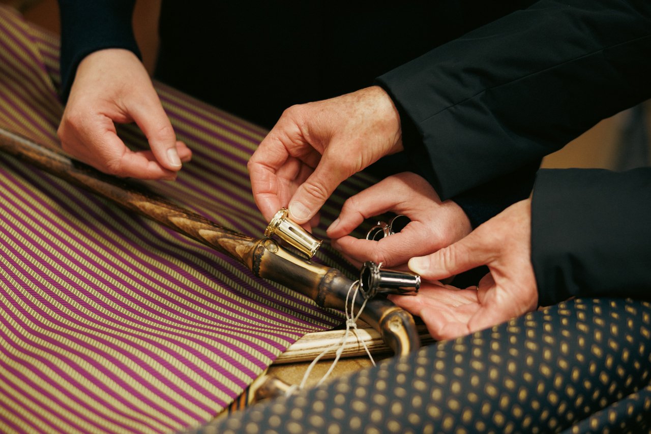 Detailed view of hands meticulously assembling the metal tip components onto an umbrella shaft.