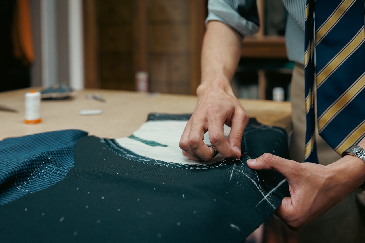 Hands carefully hand-stitching lining or interfacing onto a dark fabric piece.