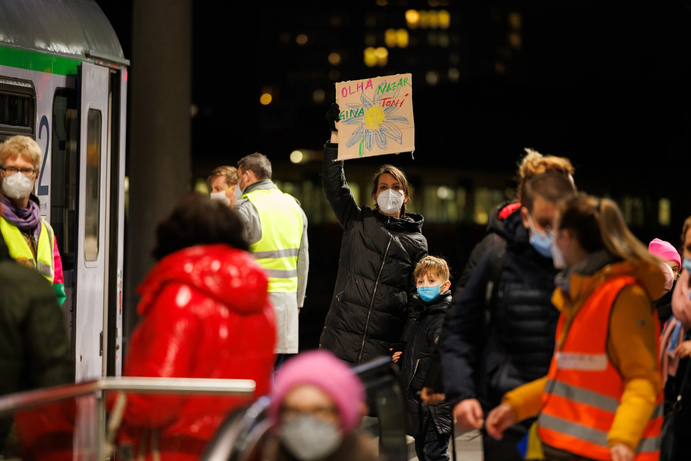 A mother and child wait with a handwritten sign for Ukrainian refugees arriving at Berlin Hauptbahnhof, March 2022