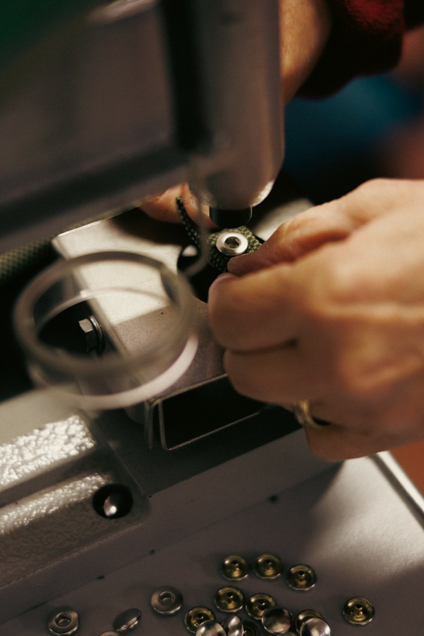 Extreme close-up of hands performing intricate mechanical work on an umbrella component, possibly using a specialized tool or machine.