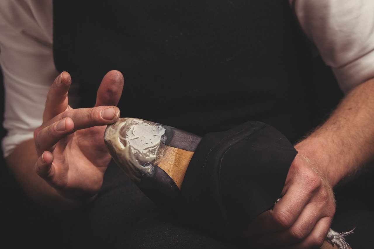 Shoemaker's hands applying adhesive or filler to the heel section of a shoe.