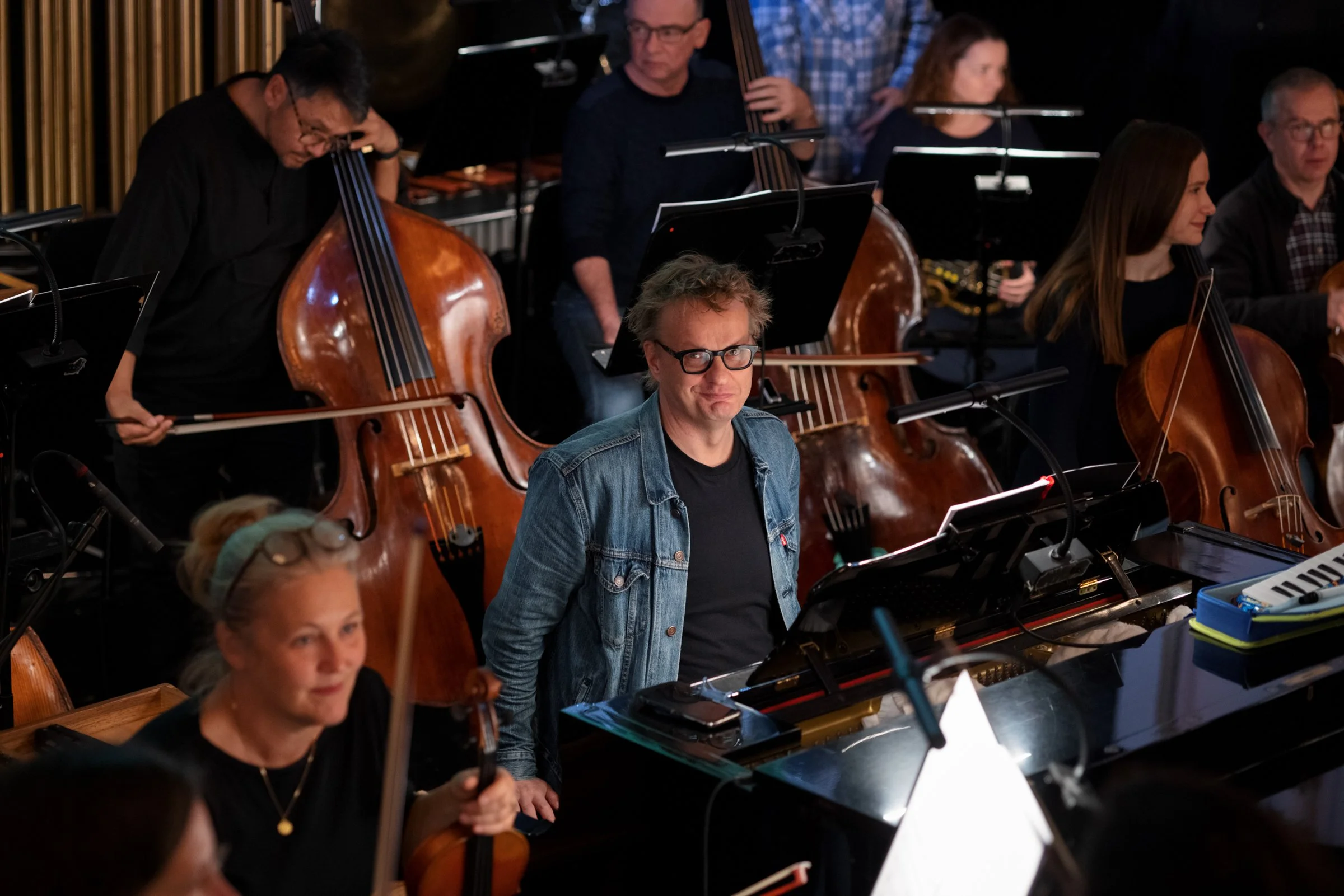 Group of musicians playing various instruments including double bass, piano, and violin during a performance in a dimly lit venue.