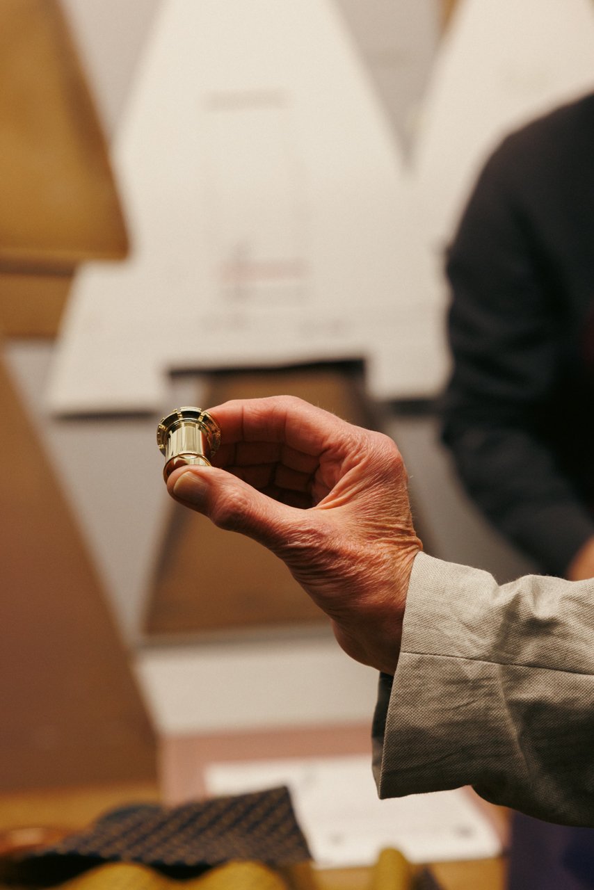 Hand holding a small, ornate metal component, likely a ferrule or part of the umbrella's tip.