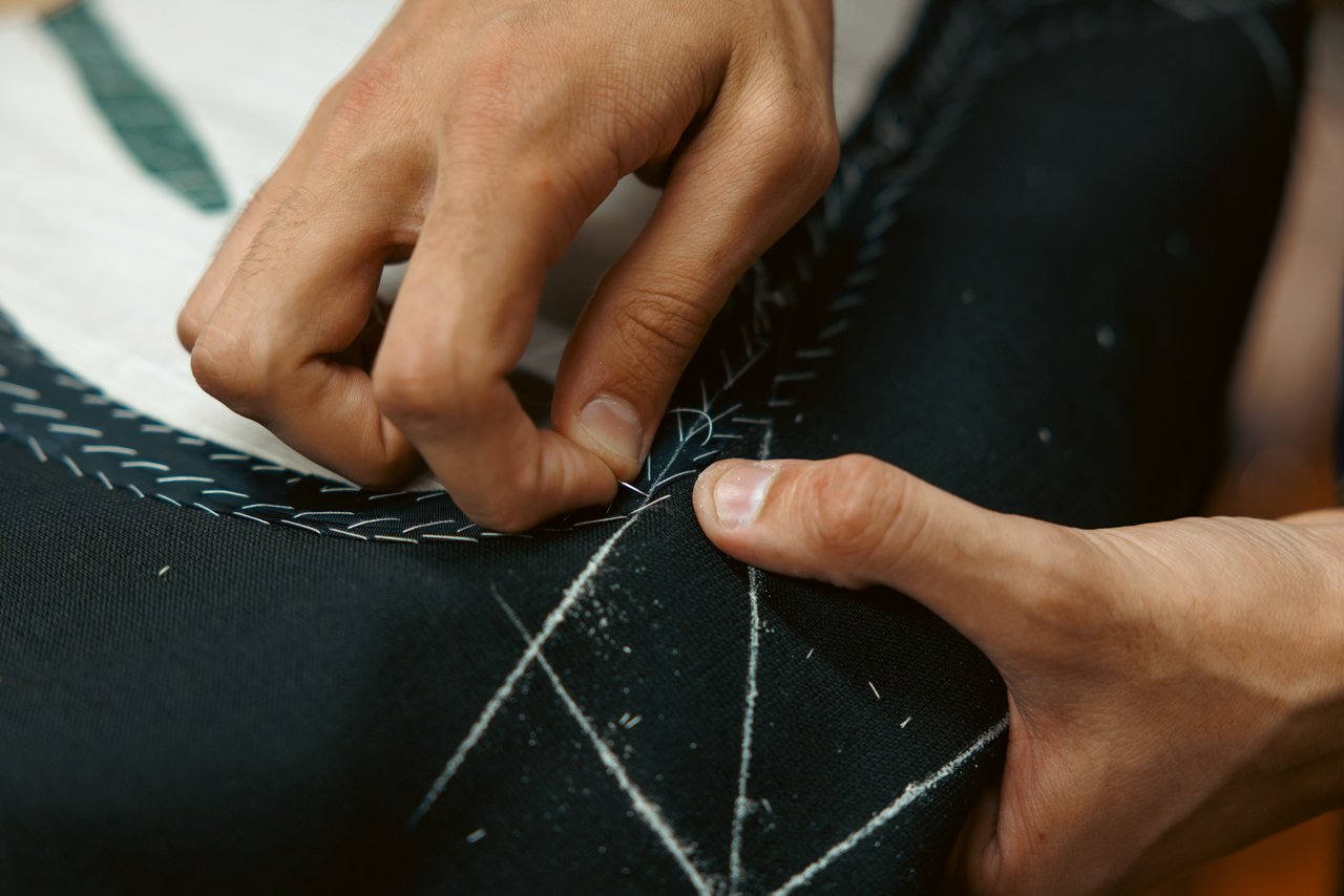 Detailed view of hands performing pick stitching along the edge of a jacket piece.