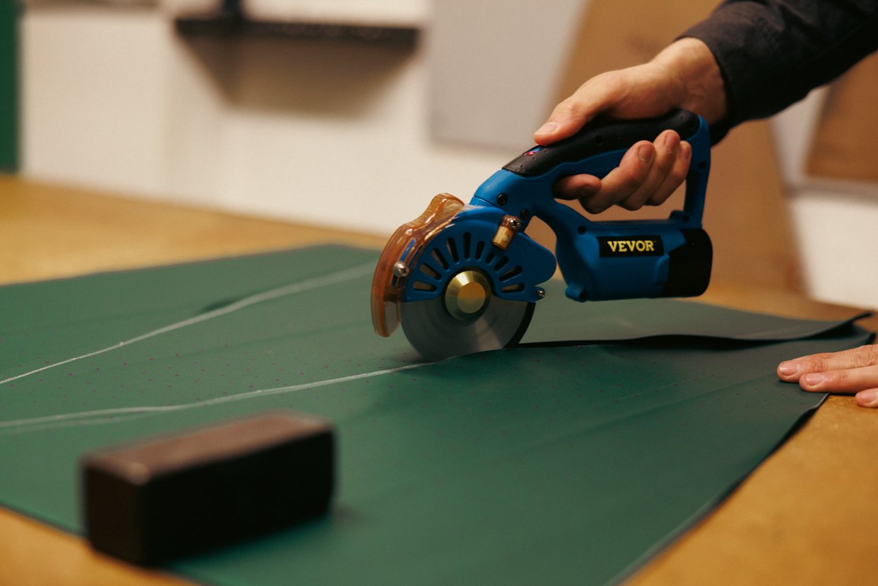 Hand guiding an electric rotary cutter precisely cutting fabric on a green mat.