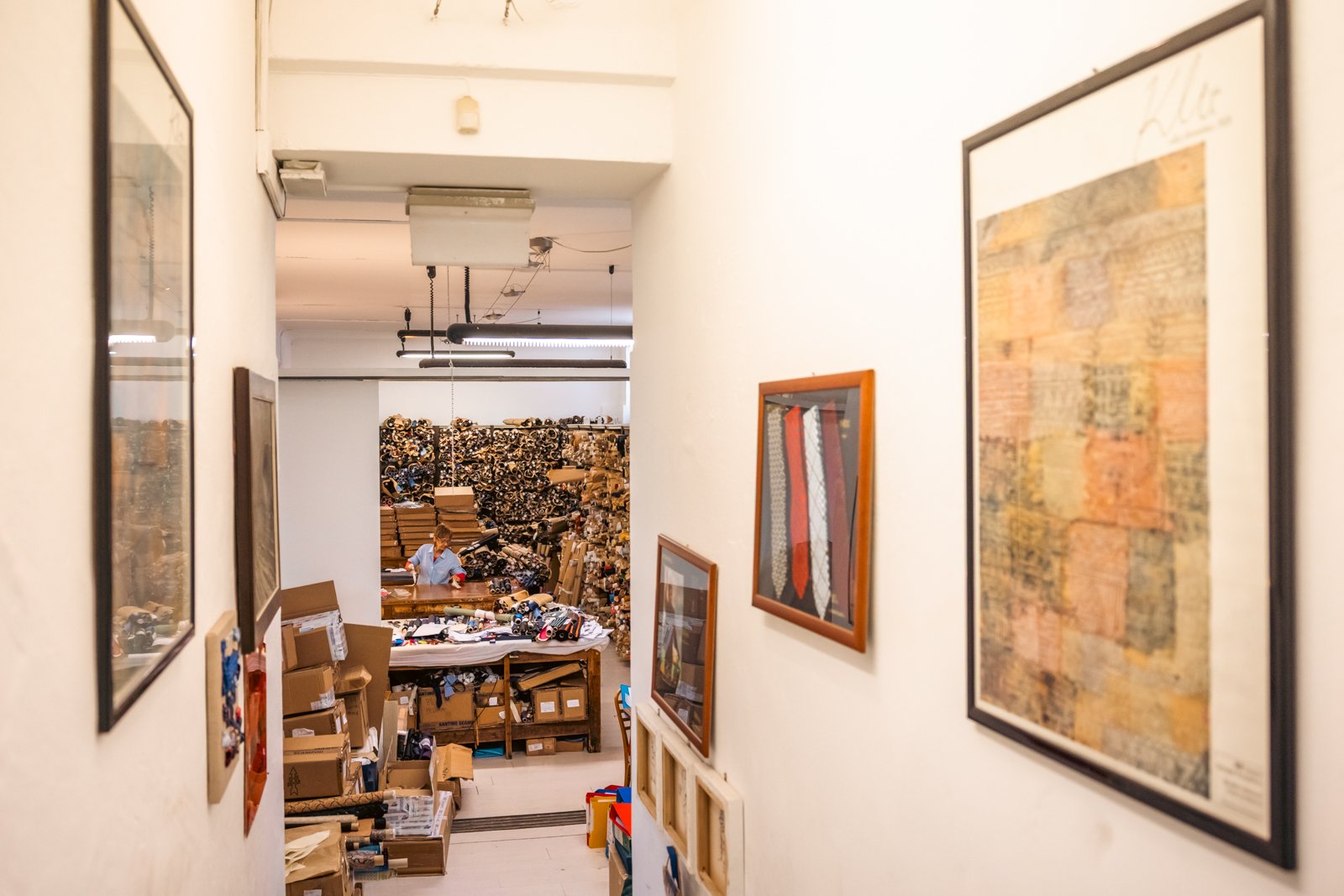 Hallway view inside the Petronius 1926 headquarters, displaying framed ties and leading towards the fabric storage area.