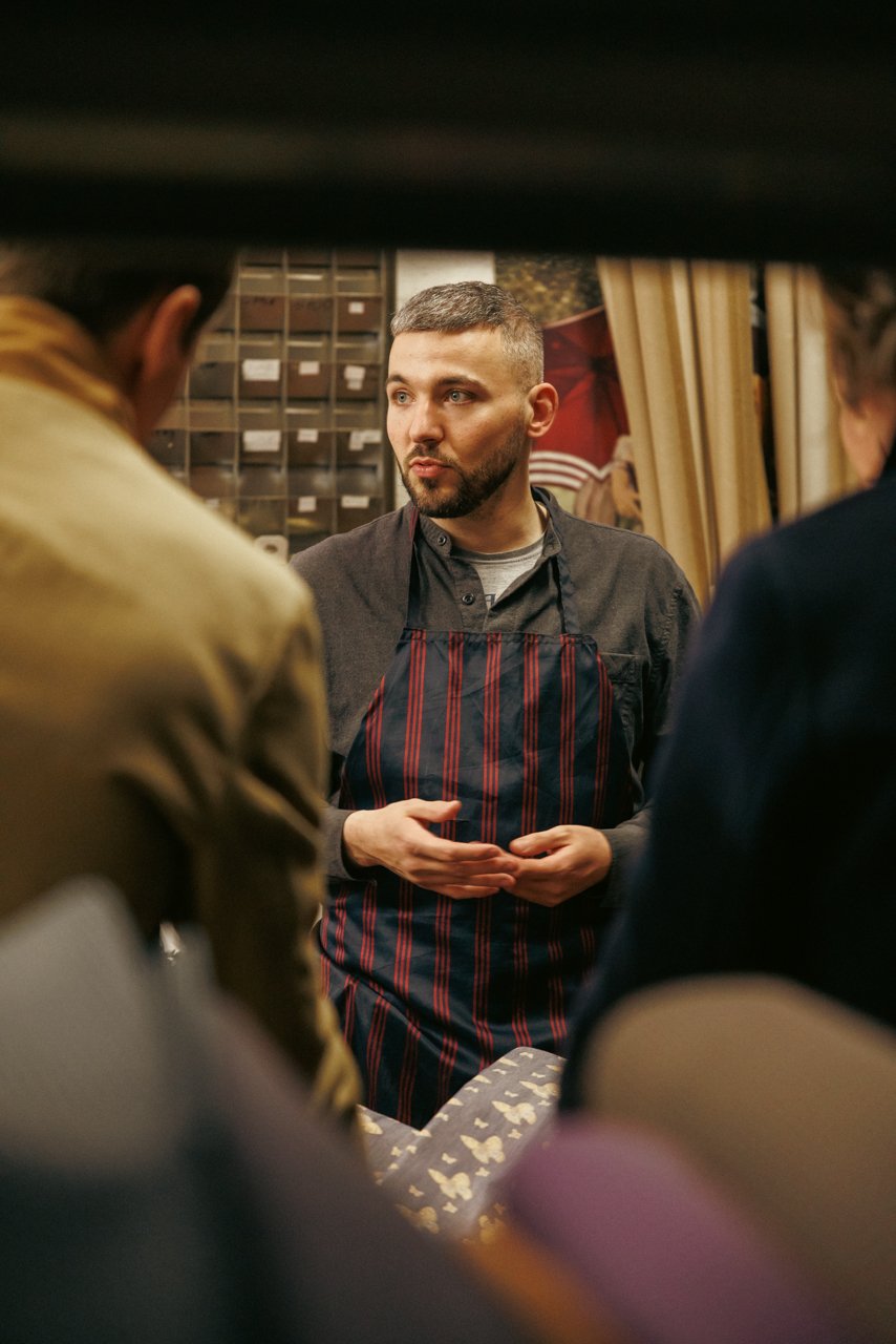 Francesco Maglia in an apron discussing details with visitors in the workshop environment.