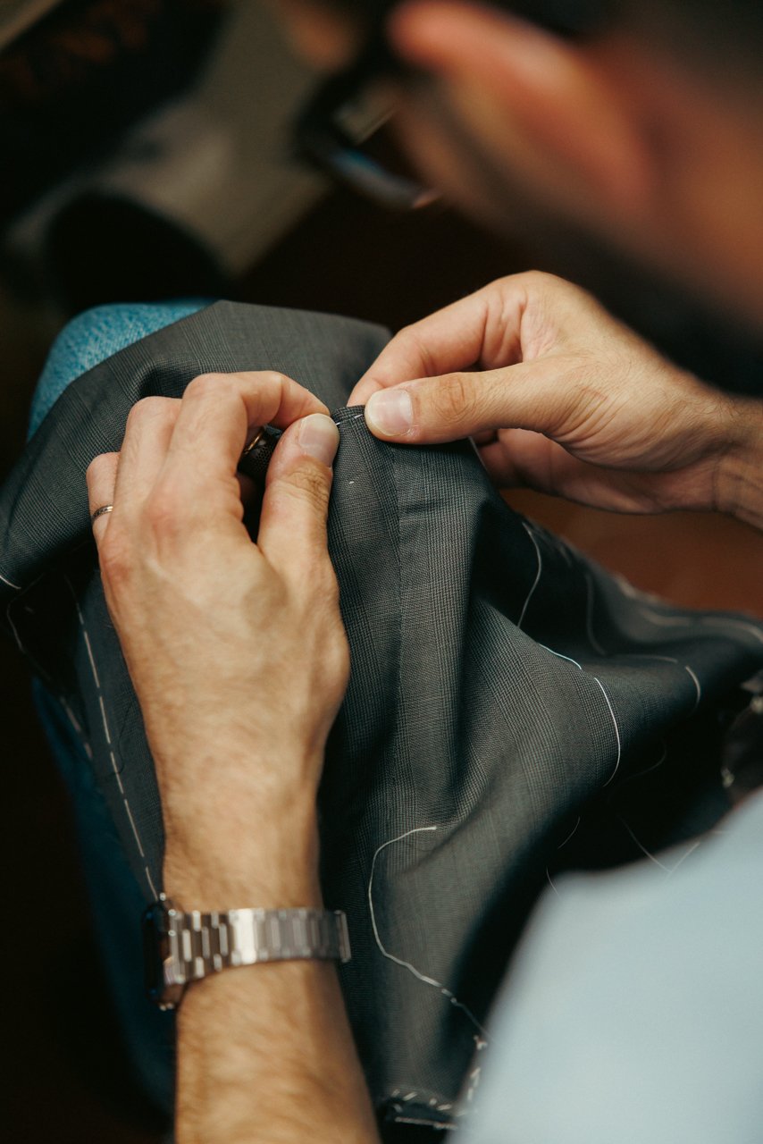 Extreme close-up of a tailor's hands executing precise hand stitches on grey fabric.