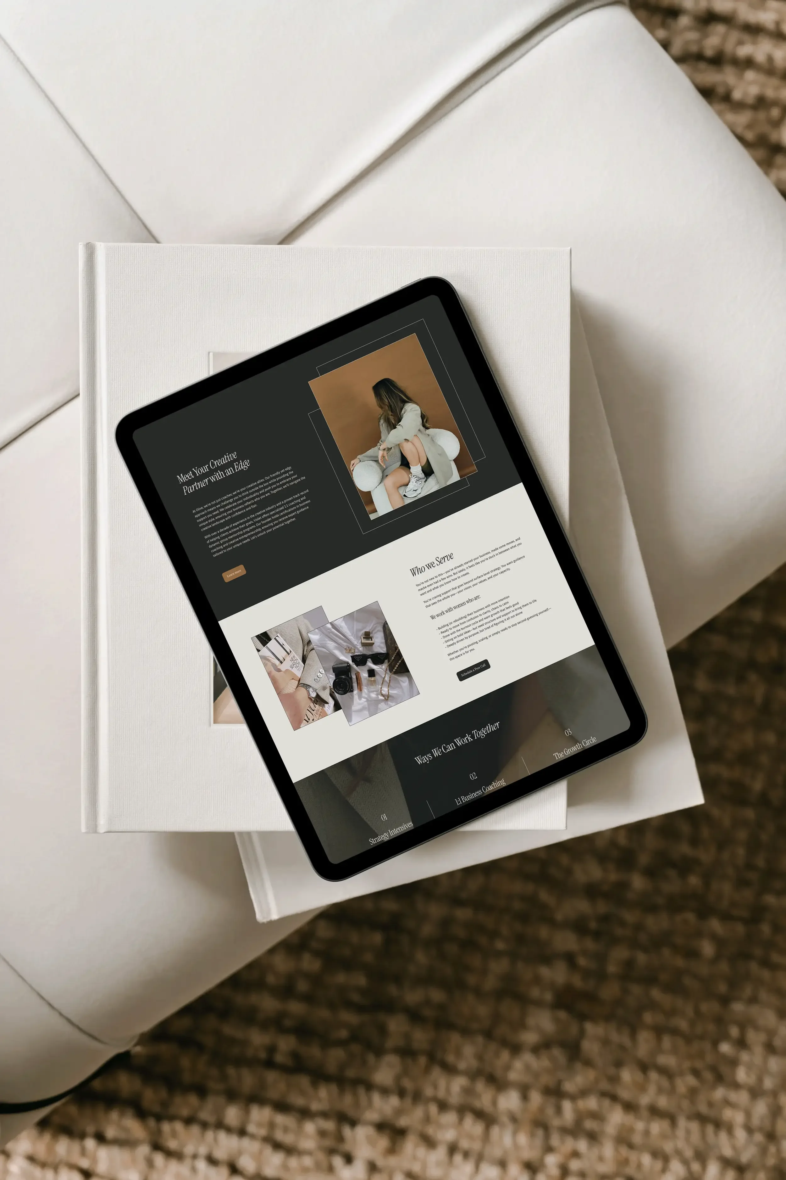Tablet displaying a webpage with a photo of a woman sitting on a white object, wearing a white coat and sneakers, and text about creative partnerships, resting on a white book on a textured brown carpet.