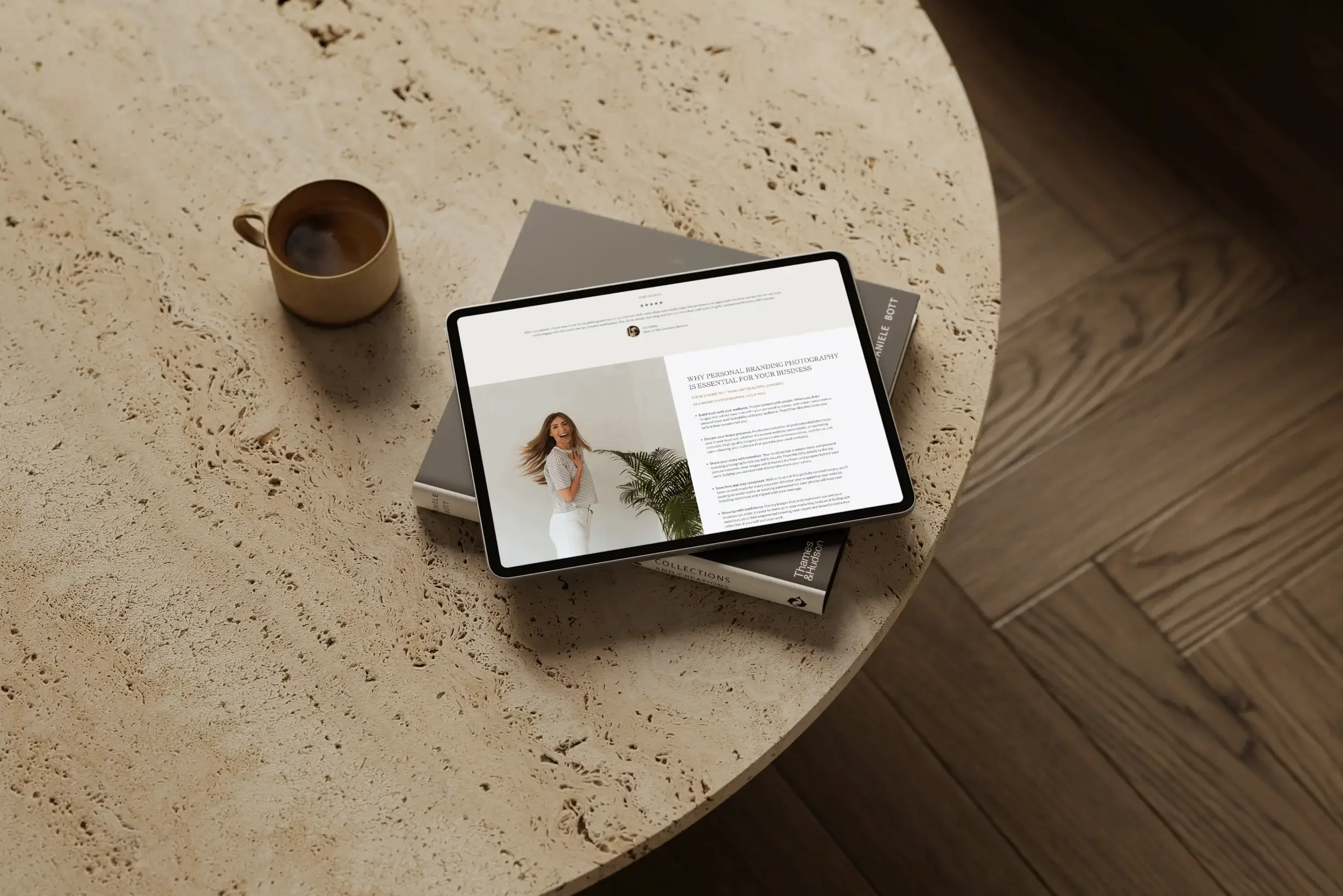 A tablet displaying a webpage about personal branding photography, a beige coffee mug, and a book, all on a textured, light-colored stone table.