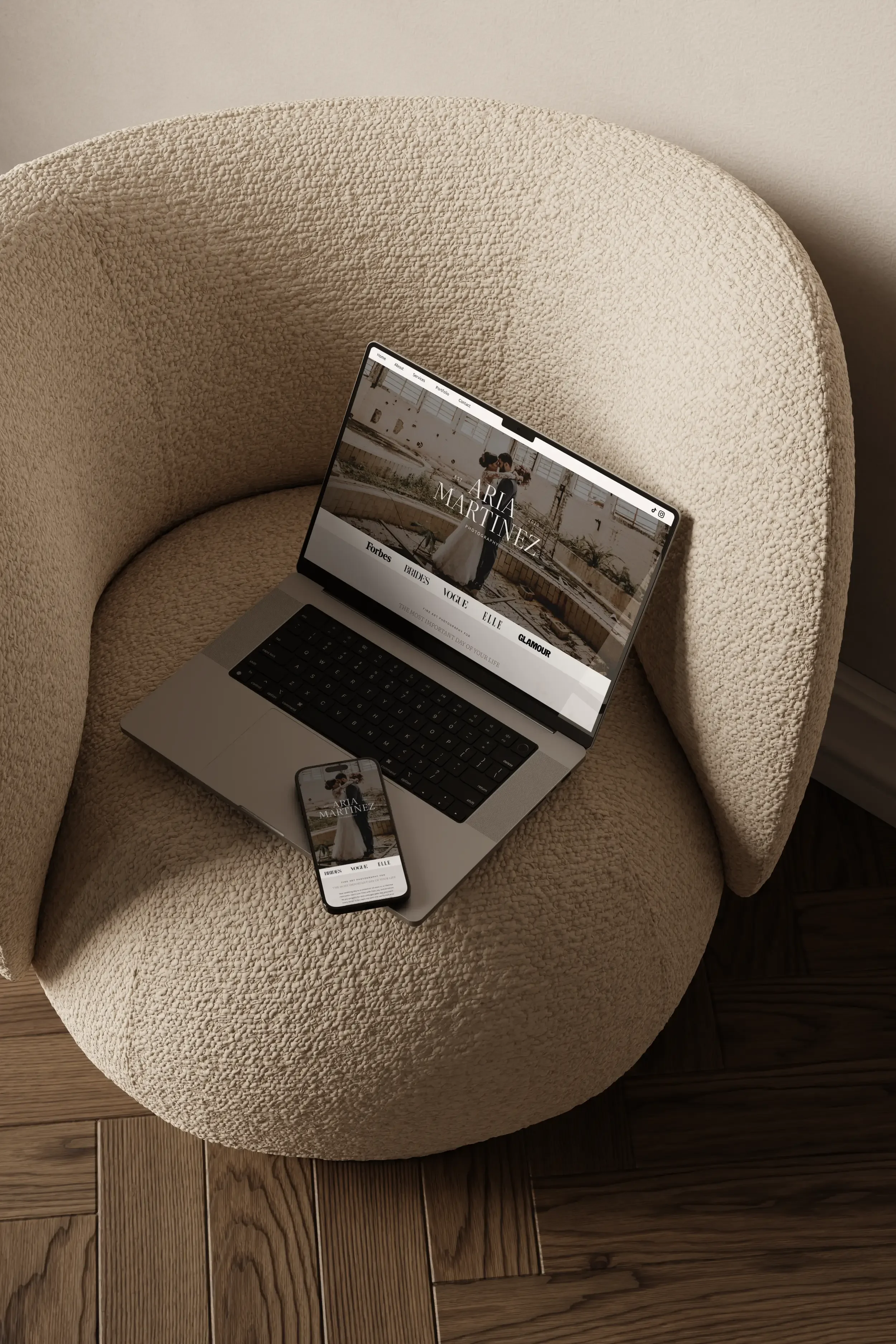 A laptop and a smartphone displaying a wedding website with the name Maria Martinez, placed on a cozy, beige, textured armchair with a rounded backrest. The armchair is on a wooden floor.