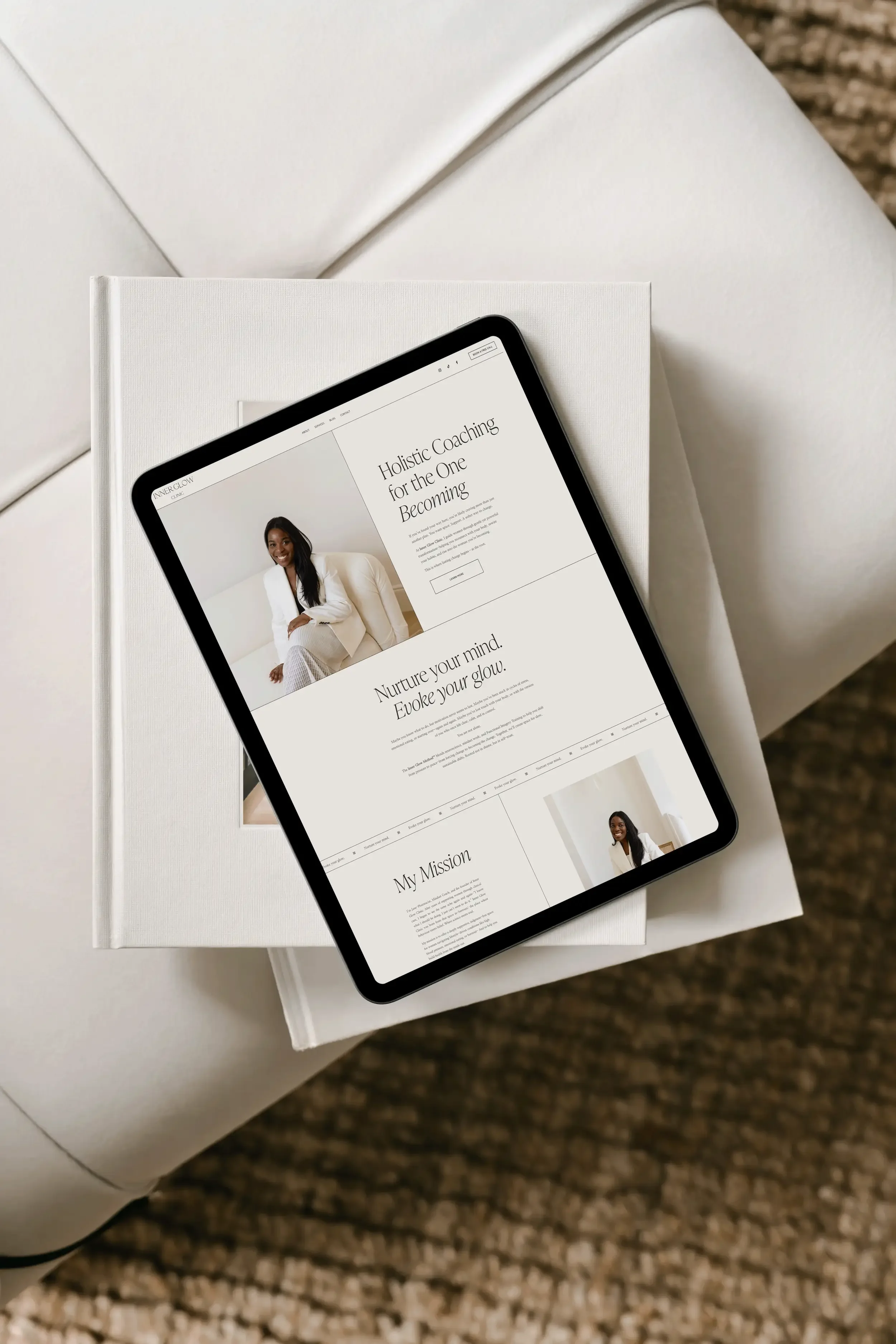 A tablet displaying a webpage about holistic coaching, resting on a closed white book on a white surface, with a textured surface beneath.