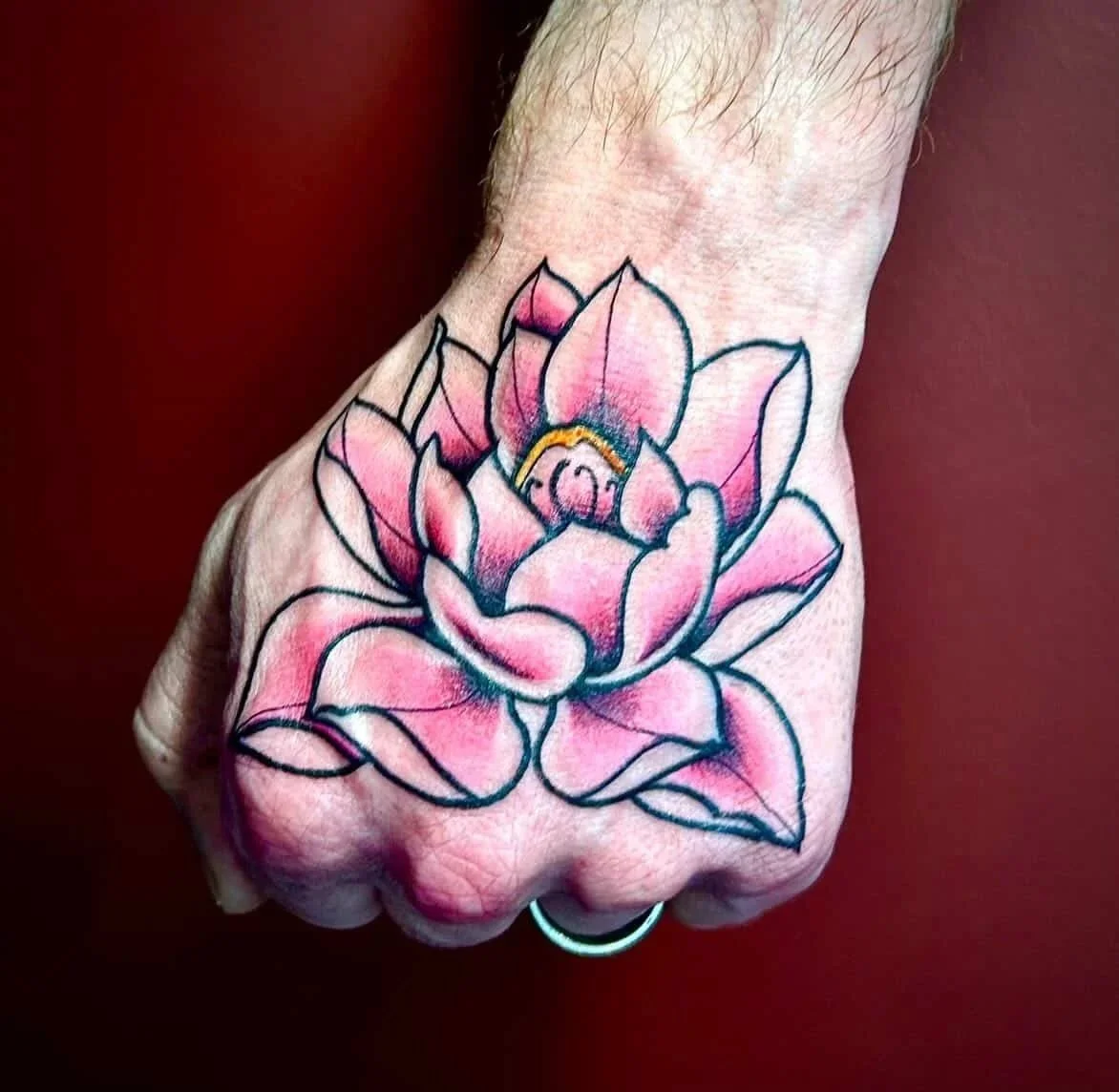 Tattoo of a pink lotus flower on a person's hand.