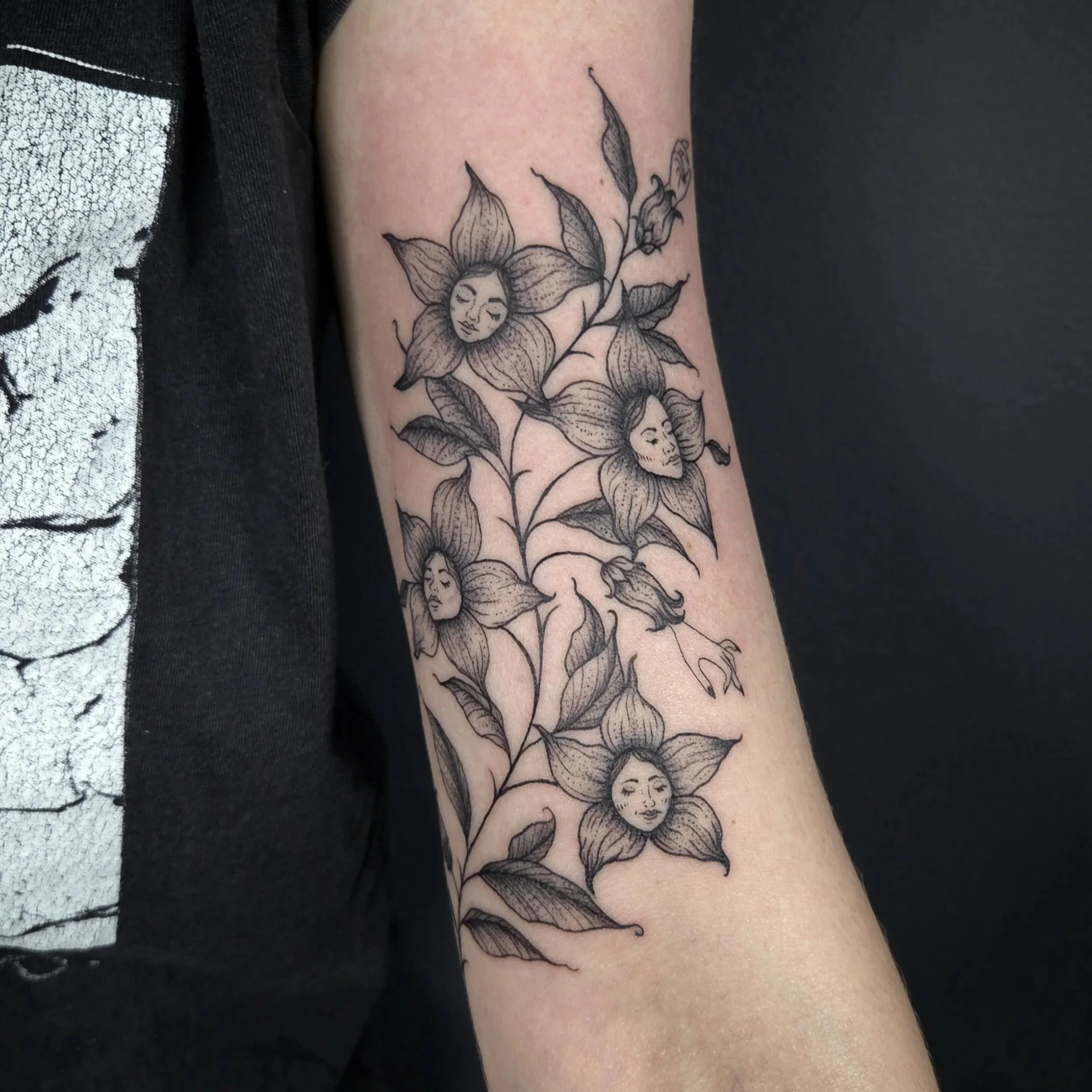 Tattoo of flowers with faces on the petals, black ink outline style.