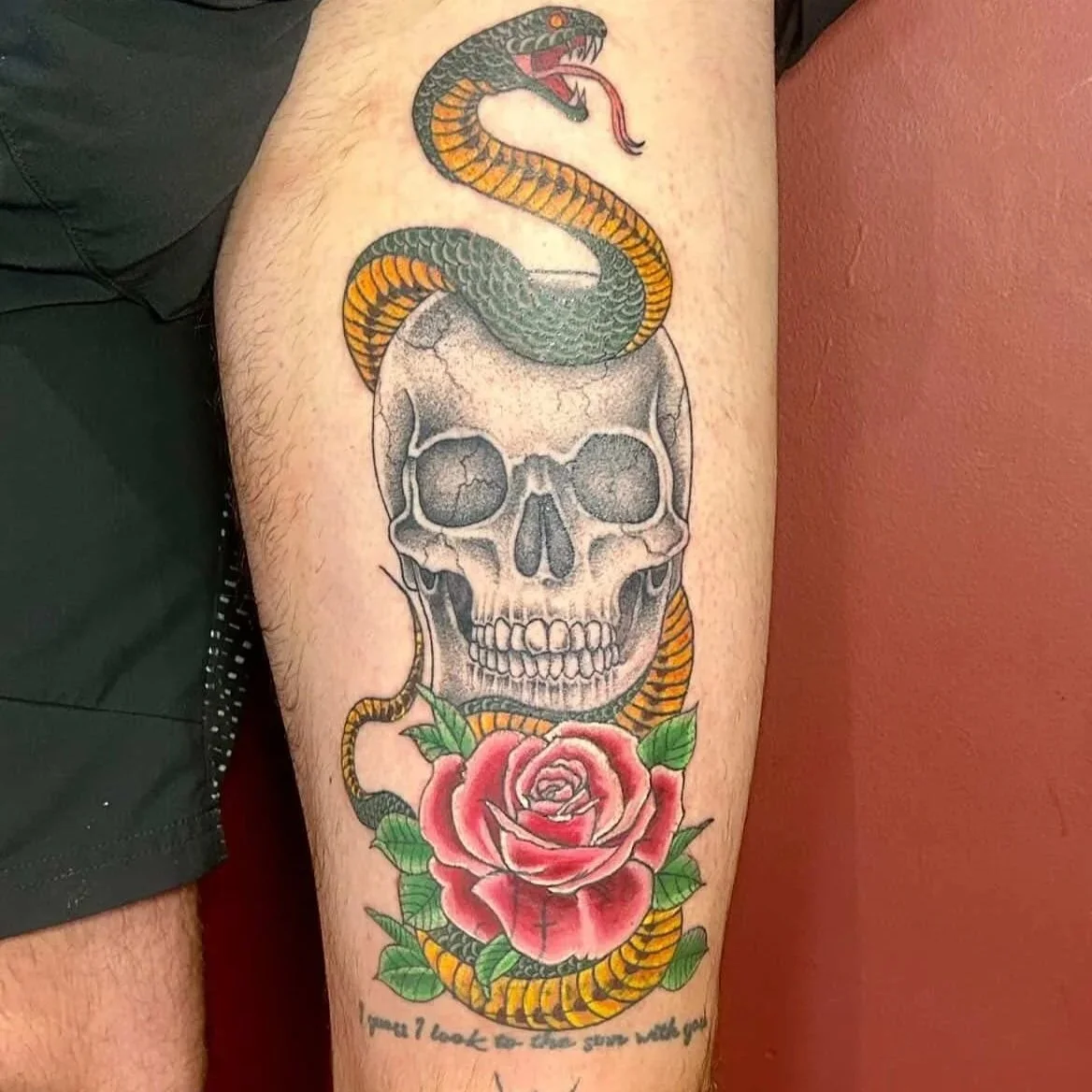 Tattoo of a skull with a snake wrapped around it and a rose at the bottom, with the text "you'll look so good when you die."