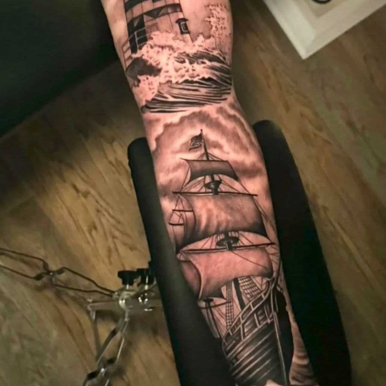 A tattoo of a sailing ship on a person's leg, with a cloudy sky and a mountain in the background.