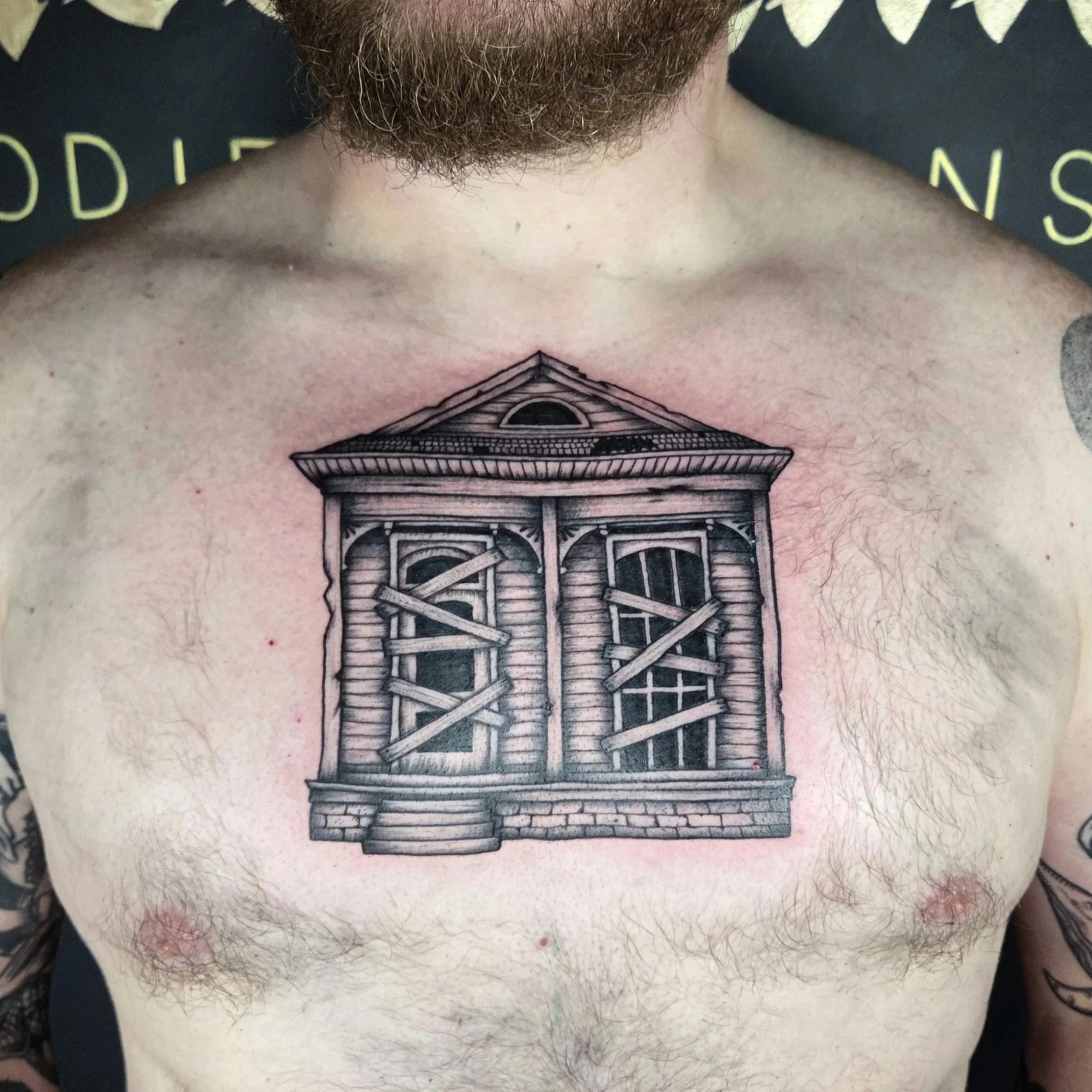 Tattoo of a boarded-up, old wooden house with steps leading up to the door, on a man's chest.