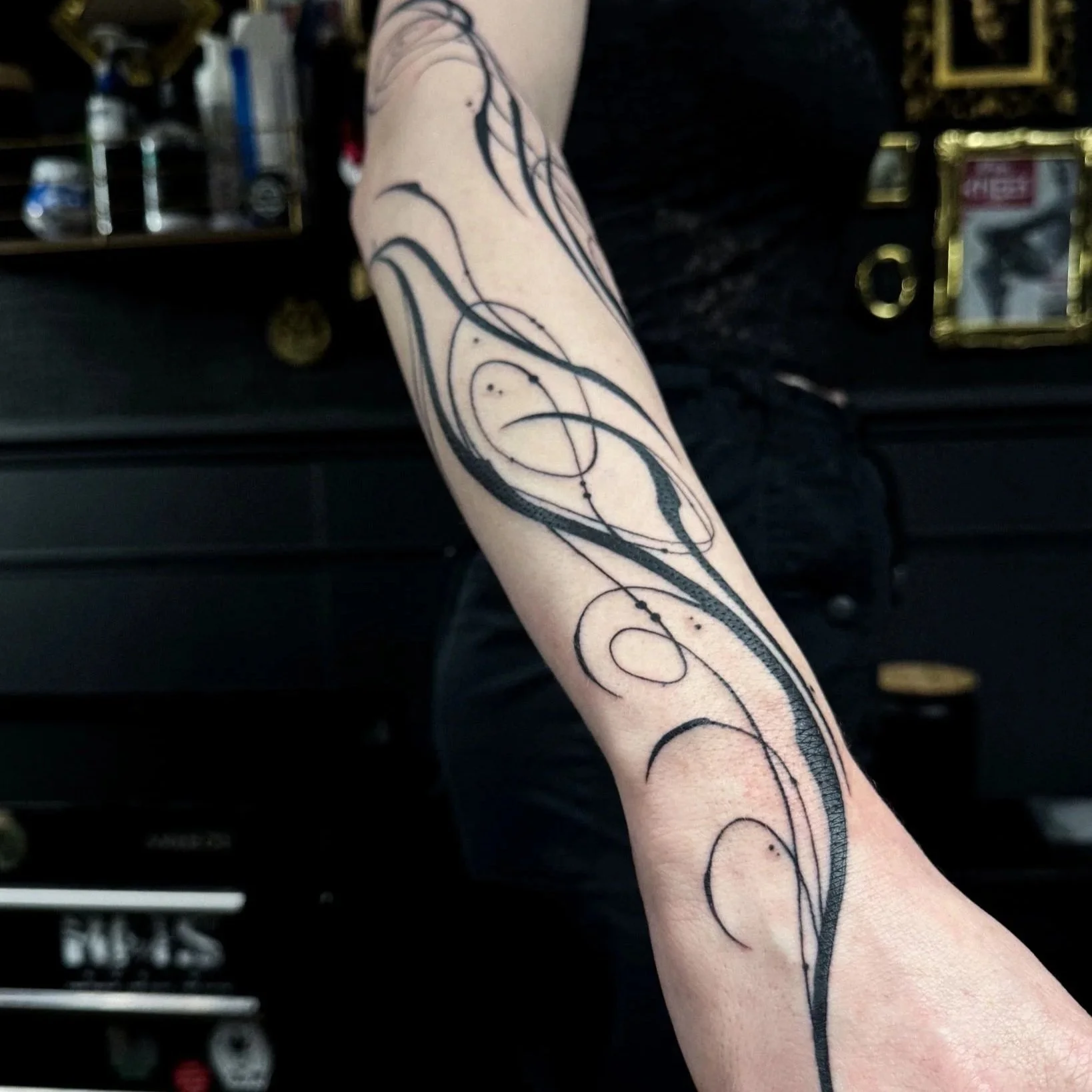 A person's forearm with a black, abstract, swirling tattoo design.