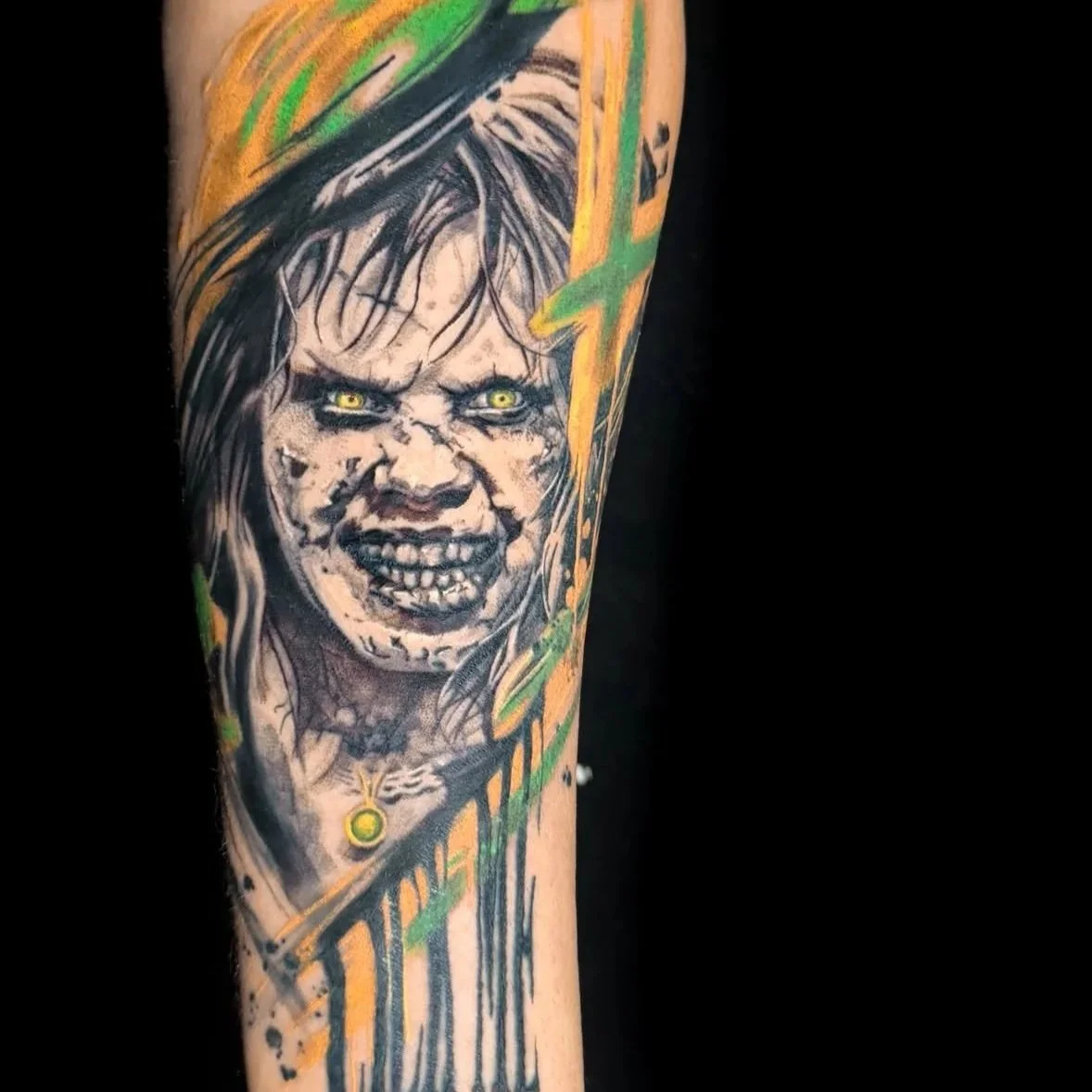 Tattoo of a fierce woman with yellow eyes, gray face, angry expression, and long hair, surrounded by green and yellow abstract lines.