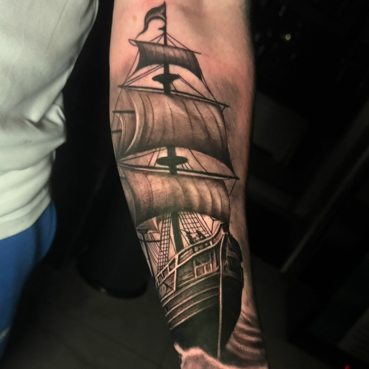 Tattoo of a sailing ship with multiple masts and sails on a person's forearm.