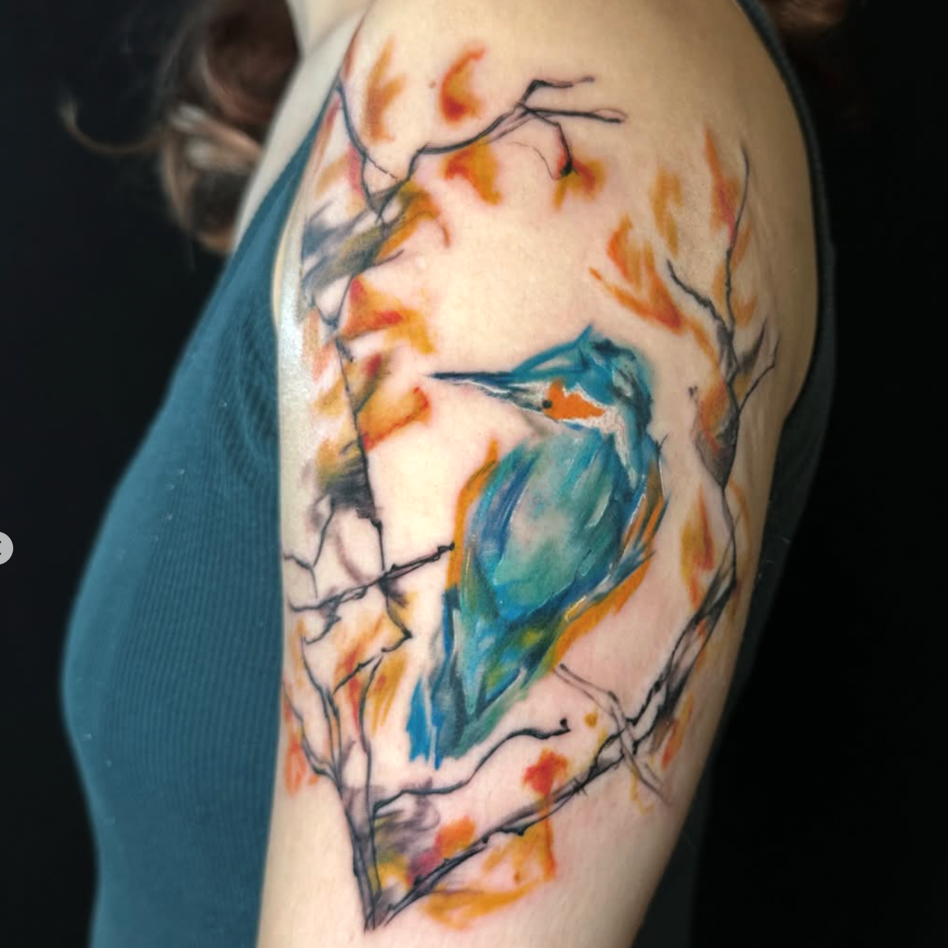 A colorful abstract tattoo of a woman with flowing hair and a hummingbird on a person's upper arm.
