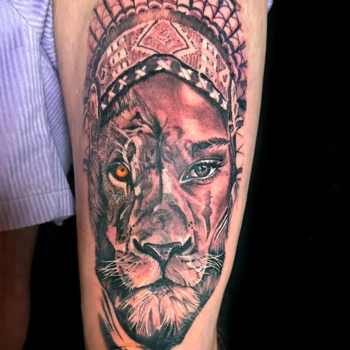 Tattoo of a lion's face with tribal patterns and a woman's face integrated, featuring detailed shading and contrasting eyes.