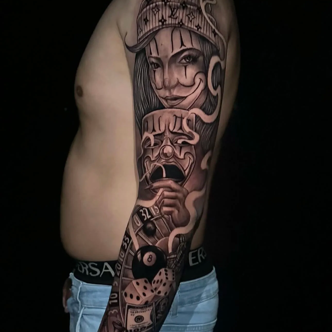 Tattoo sleeve on person's arm with a woman wearing a hat, holding a mask, dice, a billiard ball, a roulette wheel, and Poker chips in grayscale and muted colors.